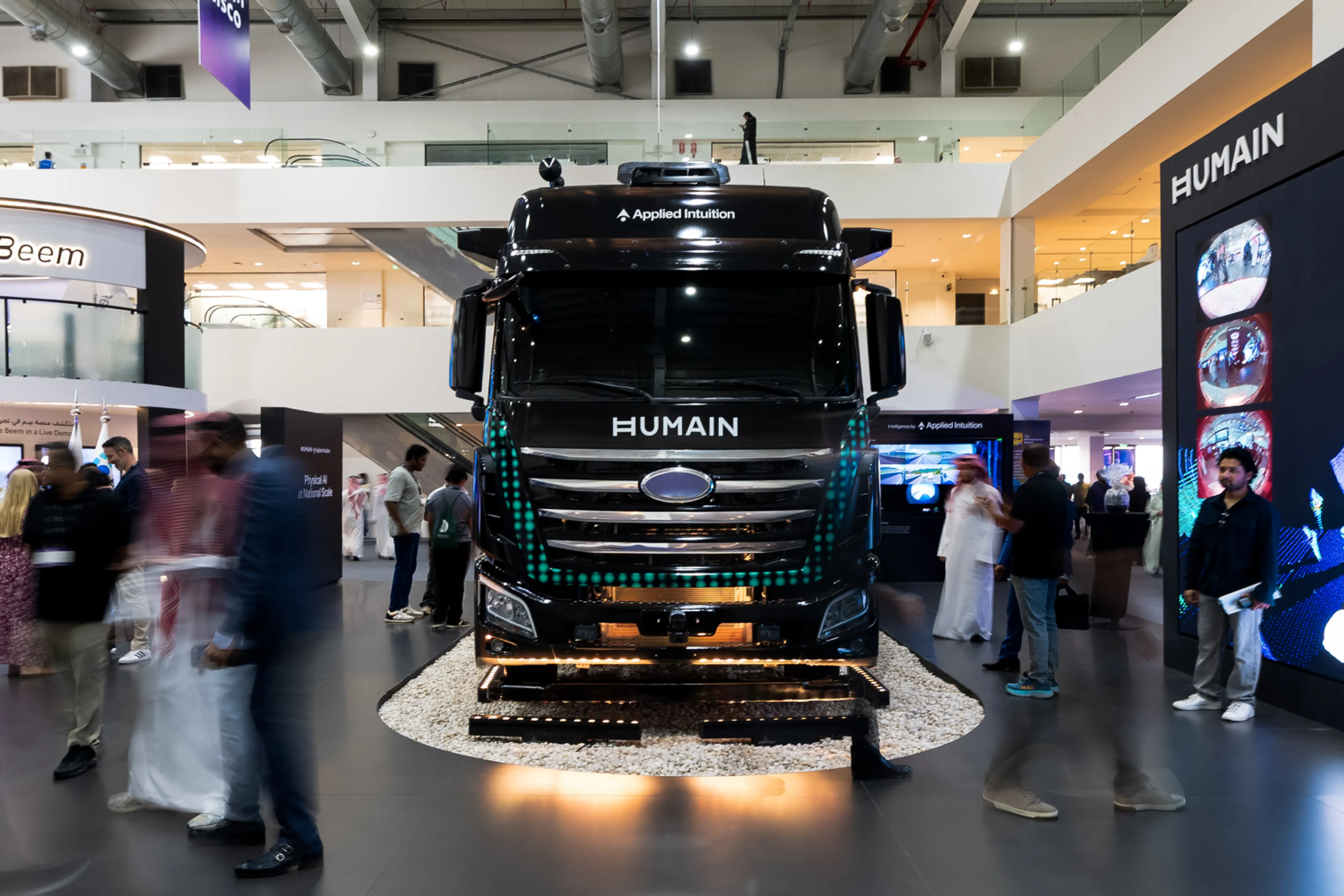 A black autonomous truck badged HUMAIN and Applied Intuition on display at LEAP 2026, with roof-mounted sensors and attendees walking past the exhibit stand.