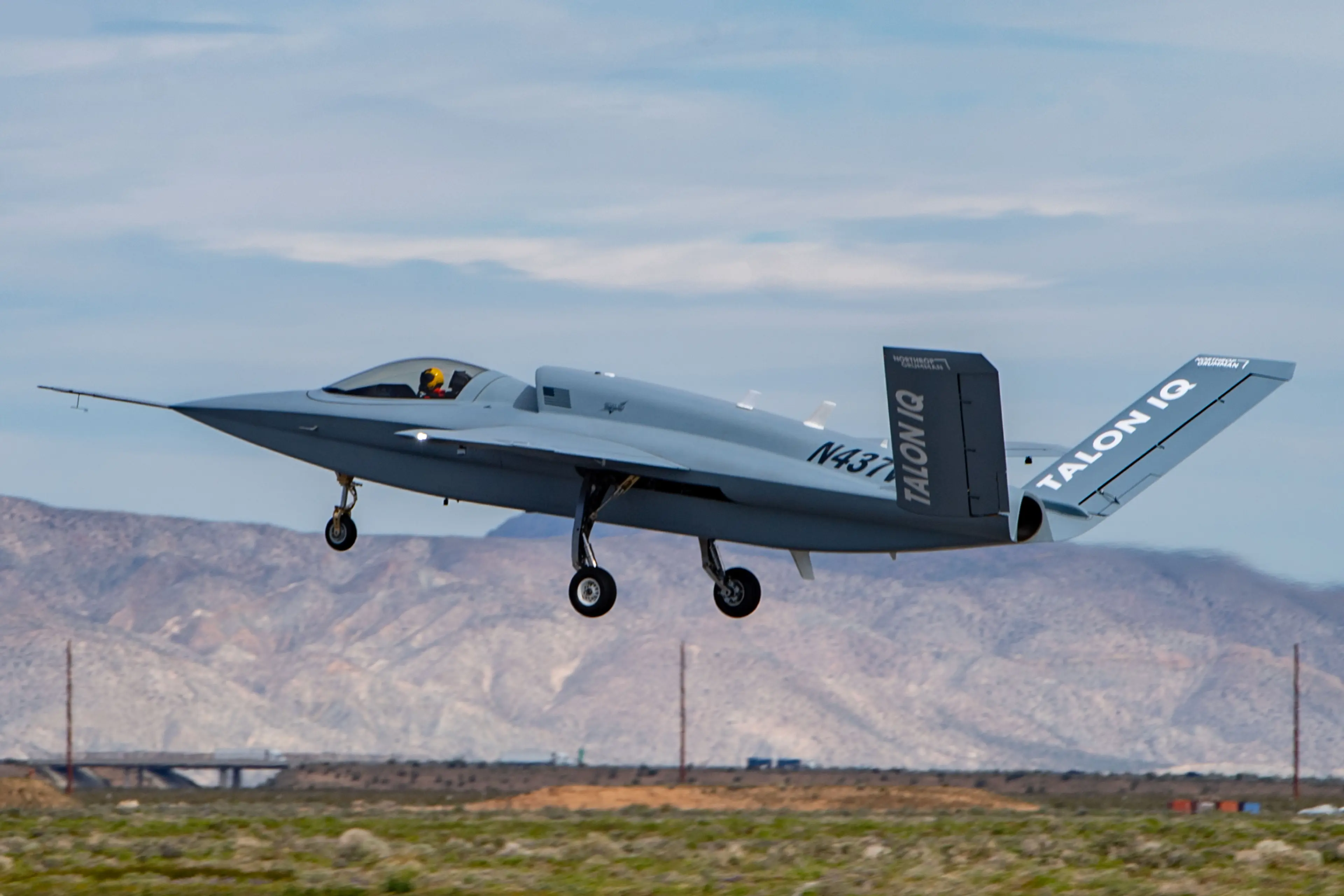 Northrop Grumman Talon IQ experimental aircraft taking off from a desert airstrip, with mountains in the background