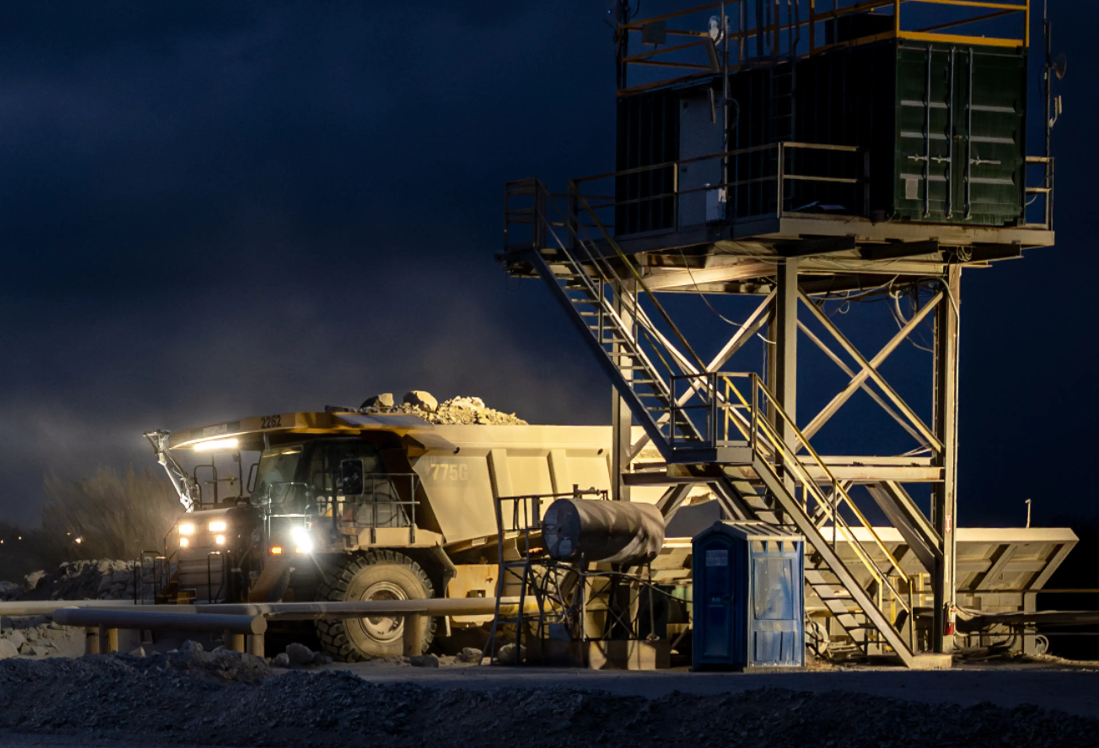 A haul truck loaded with rock passes an illuminated mine site structure at night