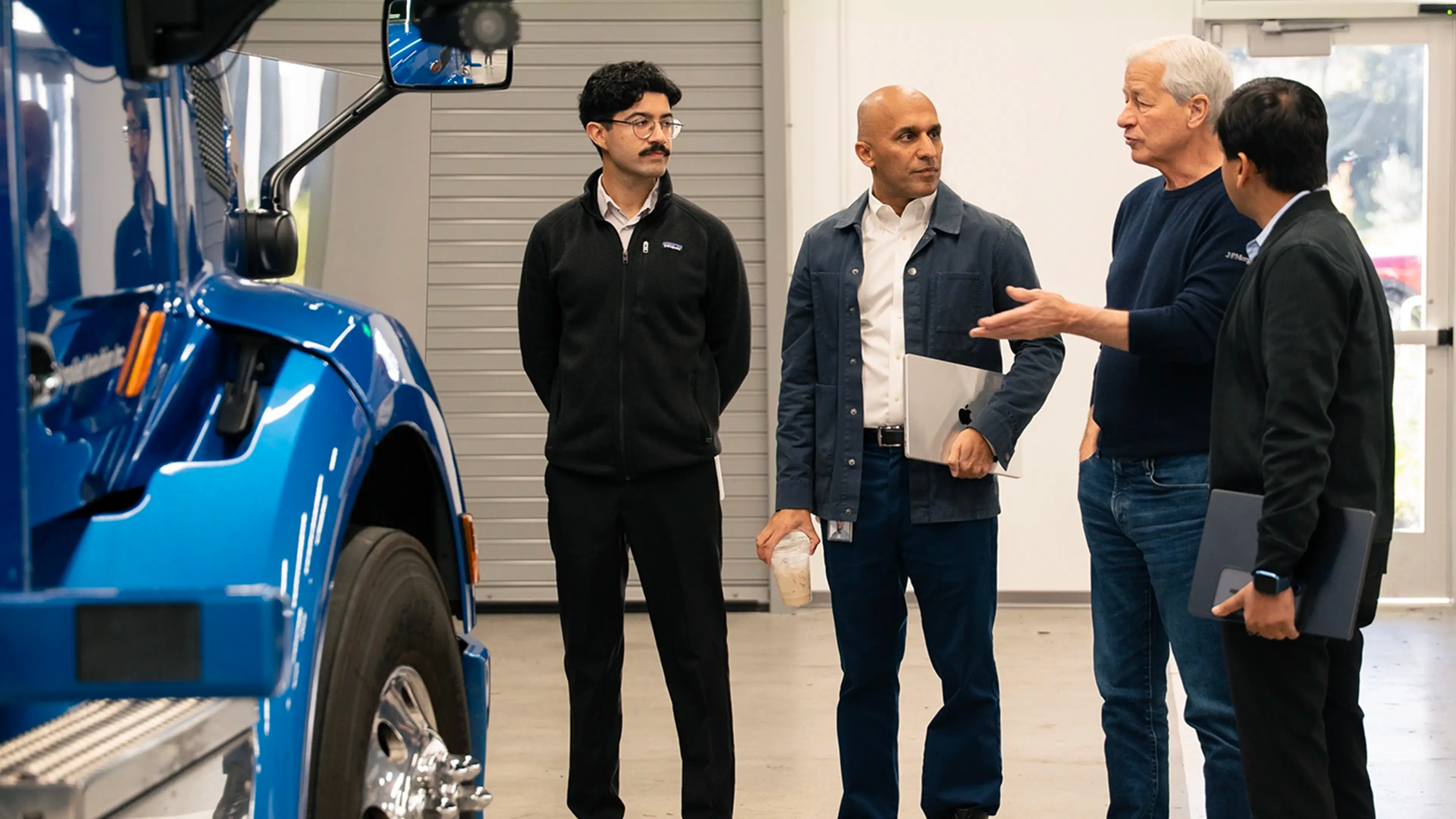 Group of executives touring a blue autonomous truck and discussing autonomous truck technology in a garage setting