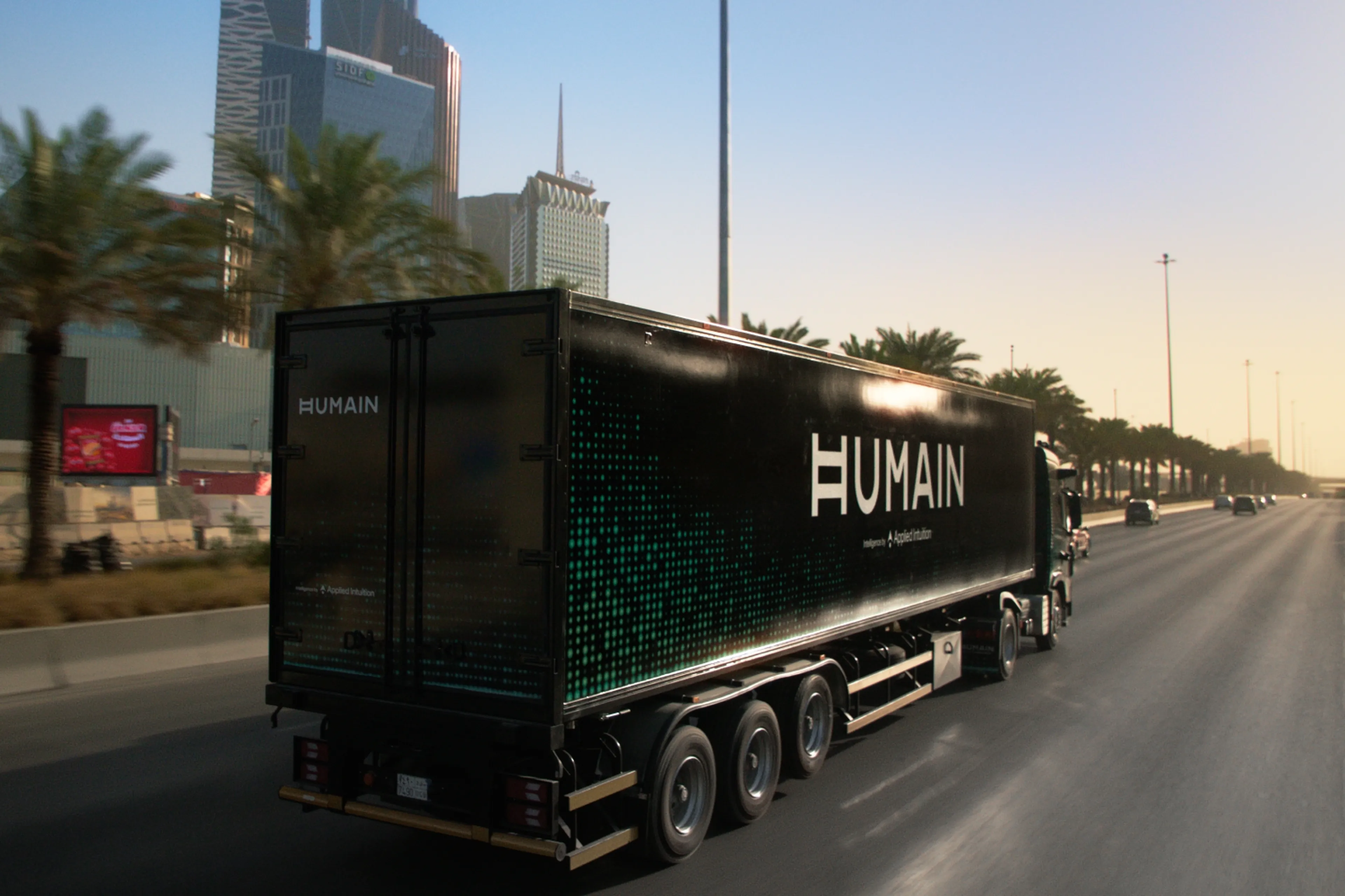 HUMAIN-branded semi-truck with Applied Intuition co-branding driving on a city highway.
