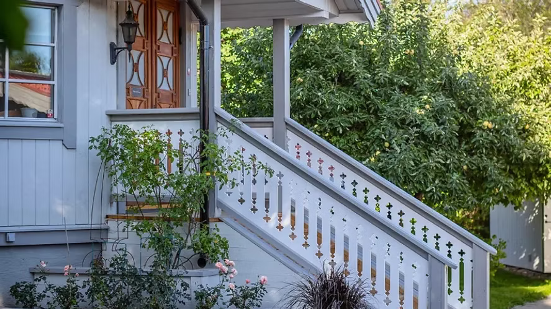 Farstukvist med utsirat vitt trappräcke, klätterrosor och blomrabatt