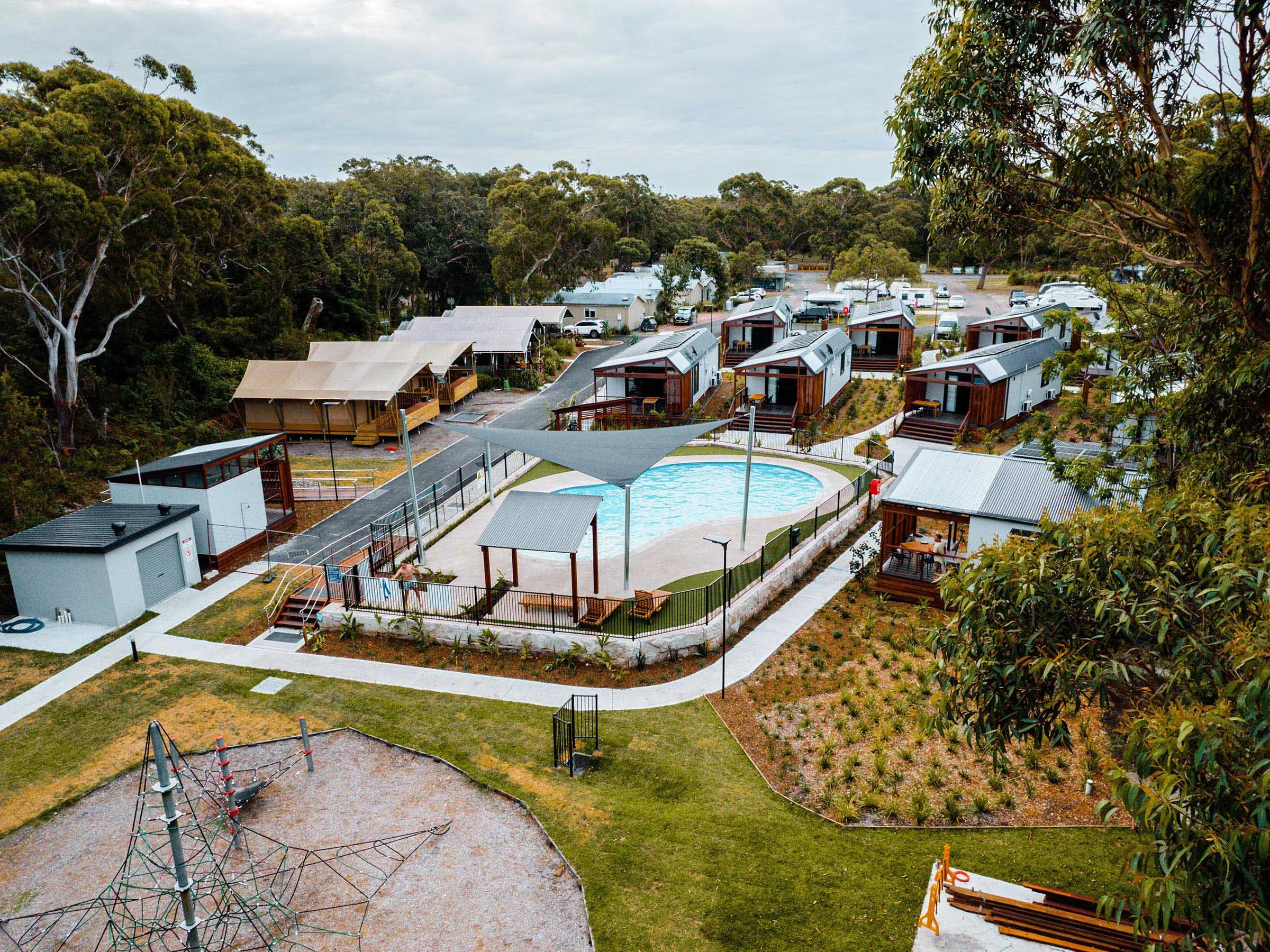 Aerial view of Reflections Jimmys Beach Caravan Park showcasing the swimming pool, modern cabins, playground, and landscaped grounds