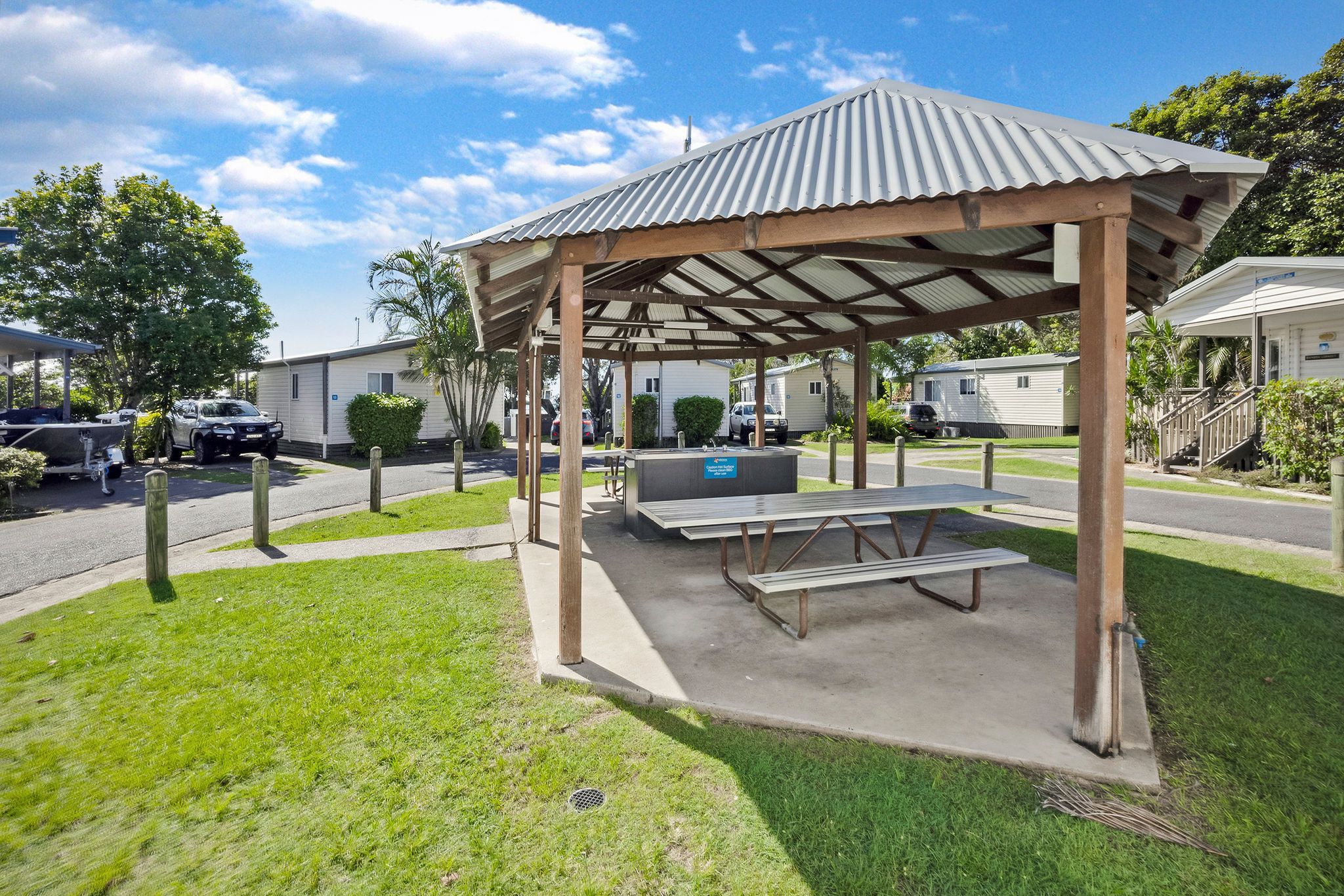 Sheltered BBQ pavilion with picnic table surrounded by green lawns at Reflections Urunga Caravan Park