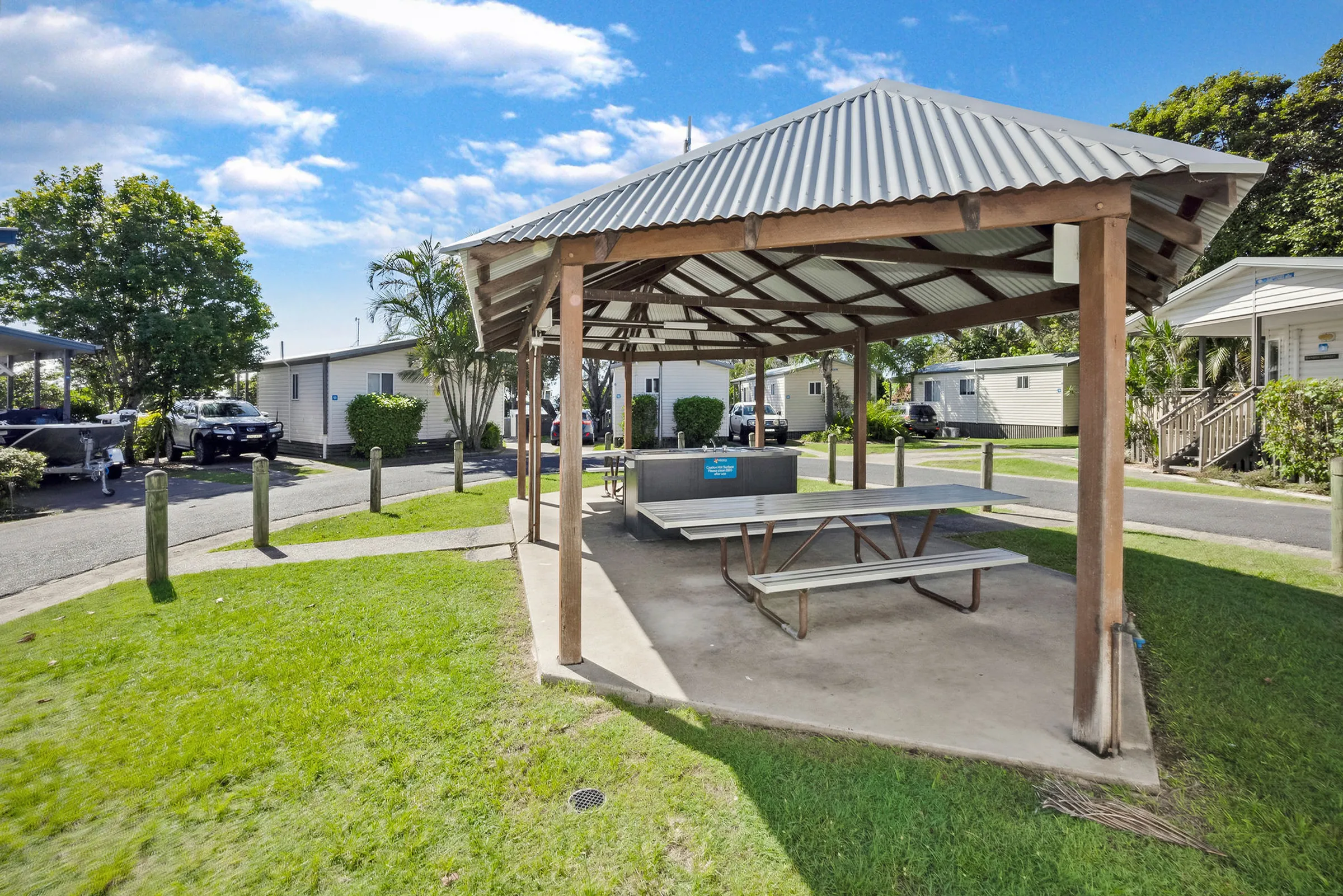 Sheltered BBQ pavilion with picnic table surrounded by green lawns at Reflections Urunga Caravan Park