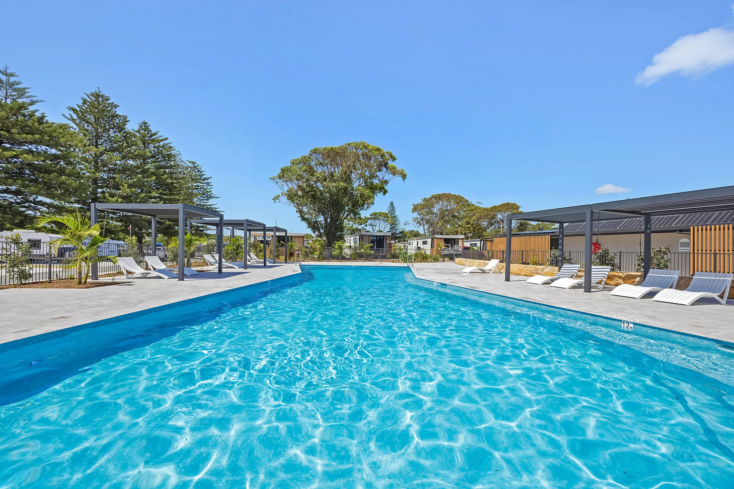 Large outdoor pool at Reflections Hawks Nest surrounded by cabanas, sun loungers, and landscaped gardens
