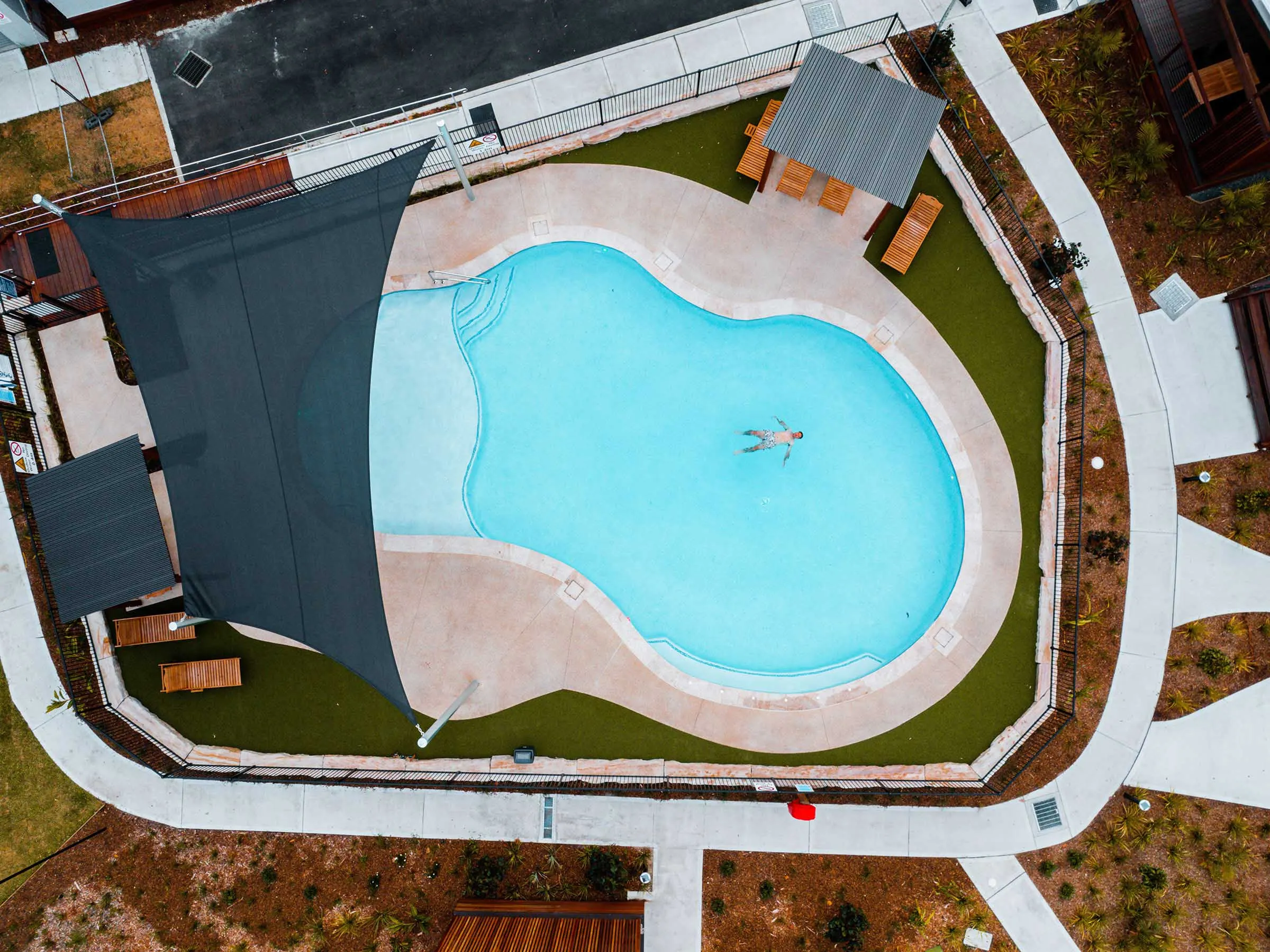 Aerial view of the swimming pool at Reflections Jimmys Beach Caravan Park, featuring a shade sail and surrounding pathways