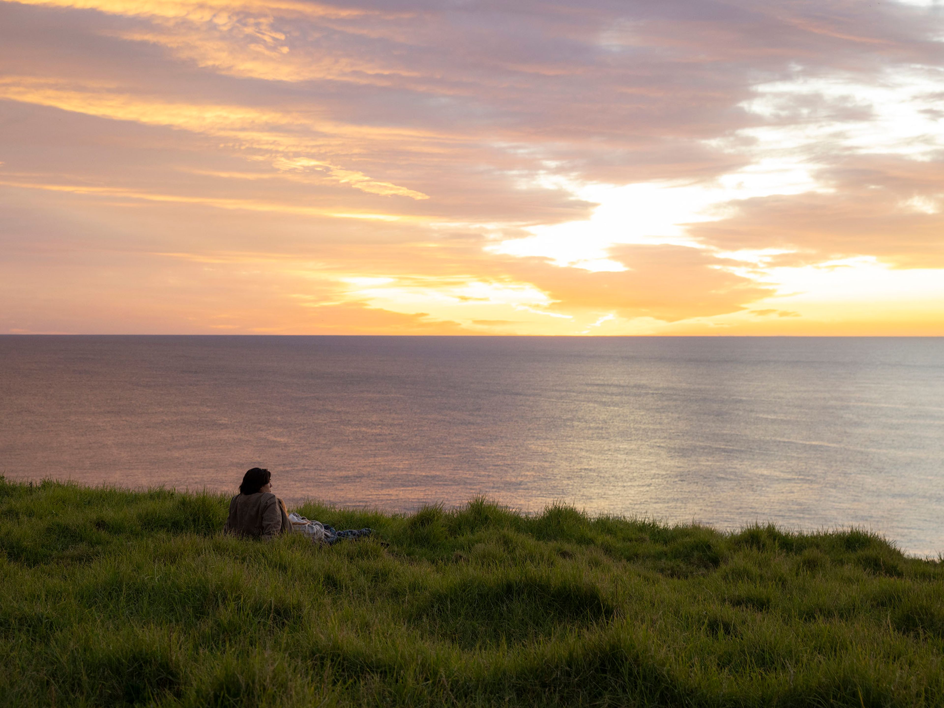 Reflections Holidays Lennox Head person looking at the South Pacific ocean relaxing on the grass over sunset