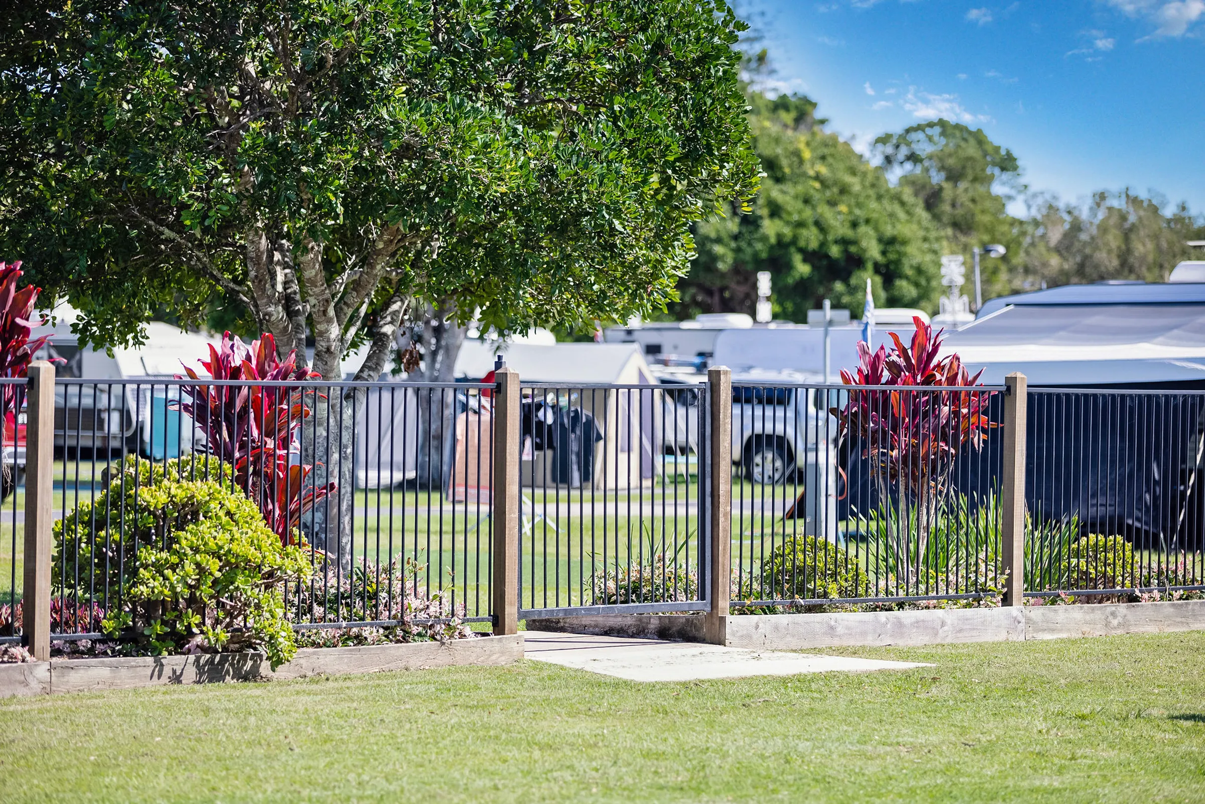 landscaped garden area with a fenced entrance at Reflections Urunga Caravan Park, to waterfront access offering a glimpse of the camping area in the background