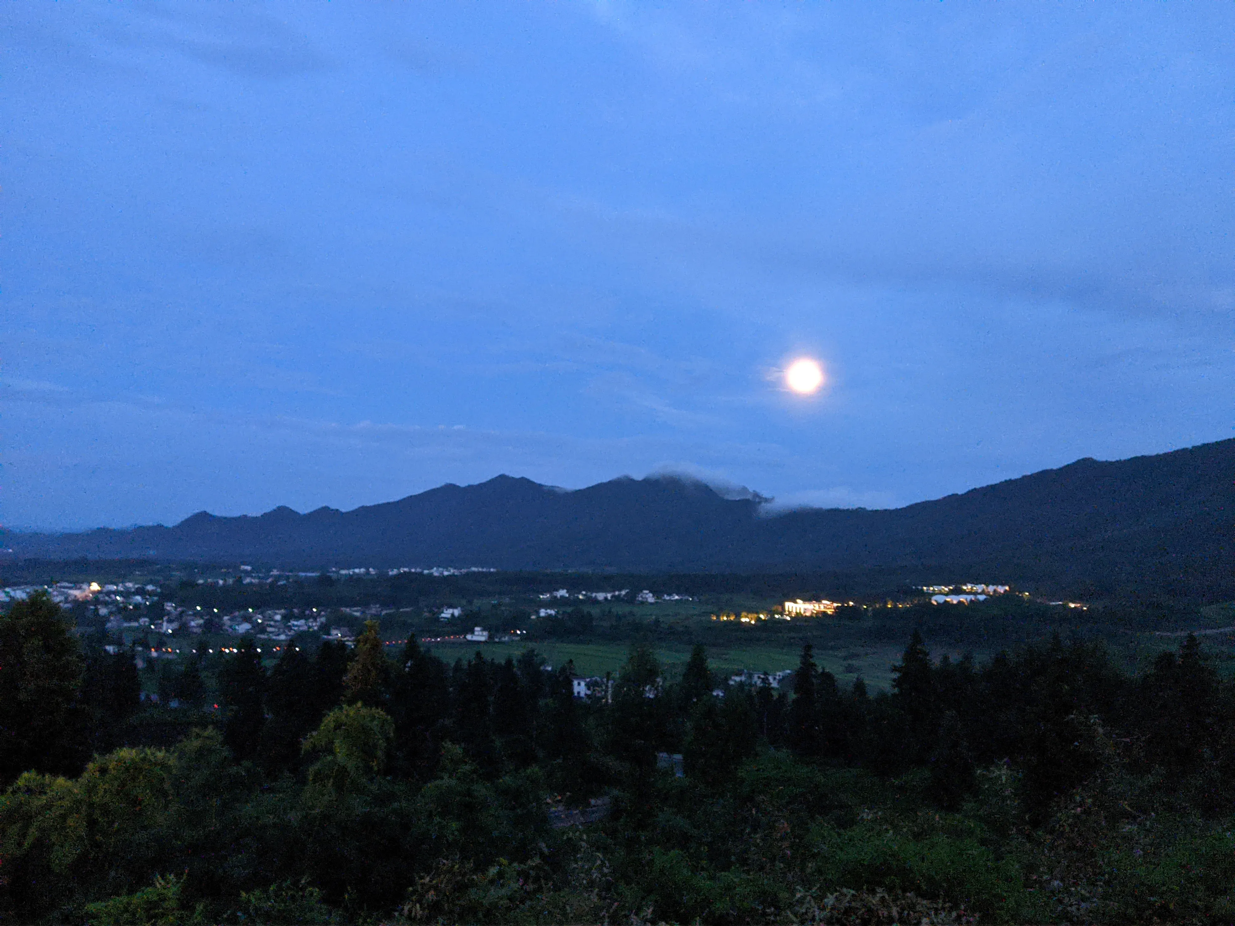 圆月升过层叠山影，村镇灯火在蓝调时刻亮起。