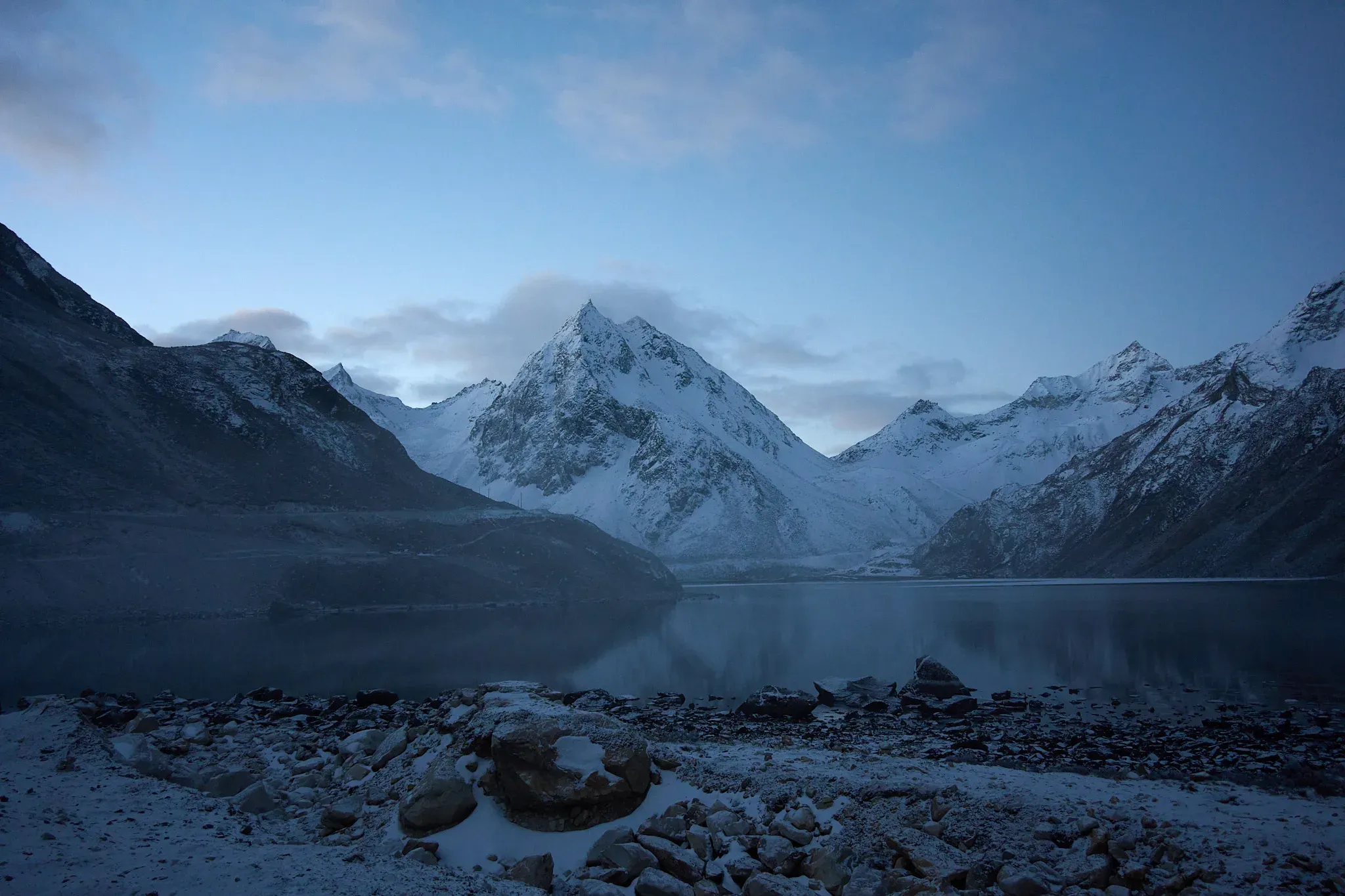 蓝调时刻的雪峰映在无风湖面，前景碎石压住冷静的远景。