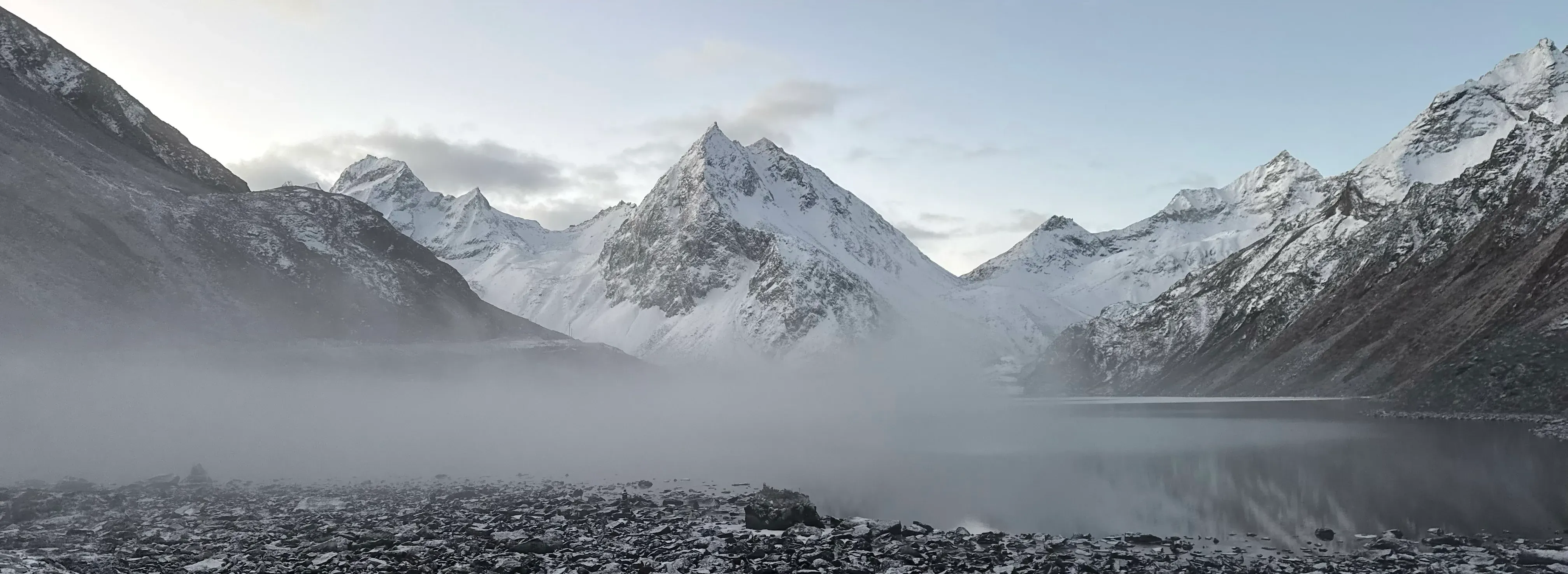 雪峰从低云之后显露，碎石河谷横贯画面。