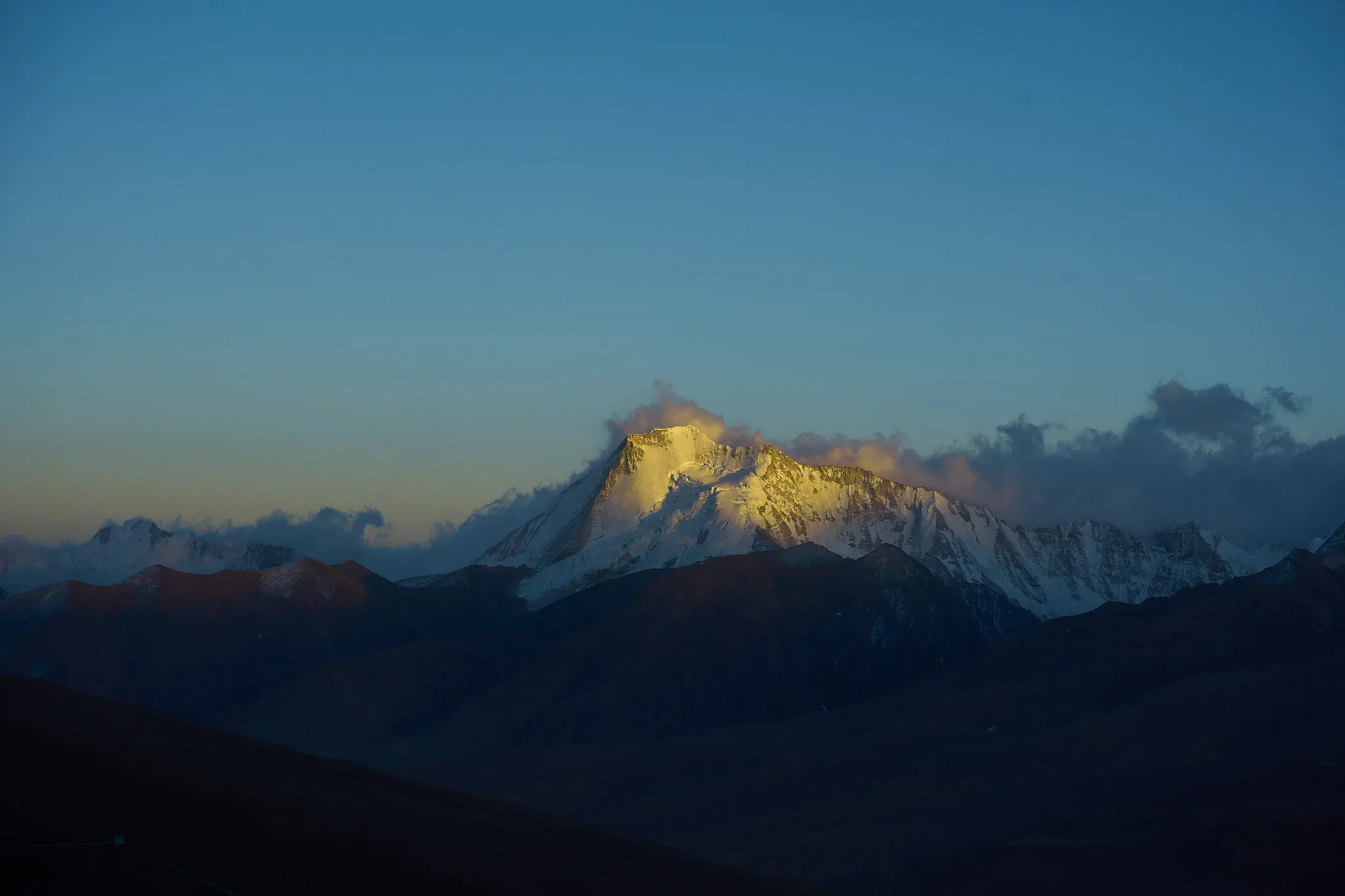 晨昏金光只落在雪峰顶部，山脚仍沉在深蓝色阴影里。
