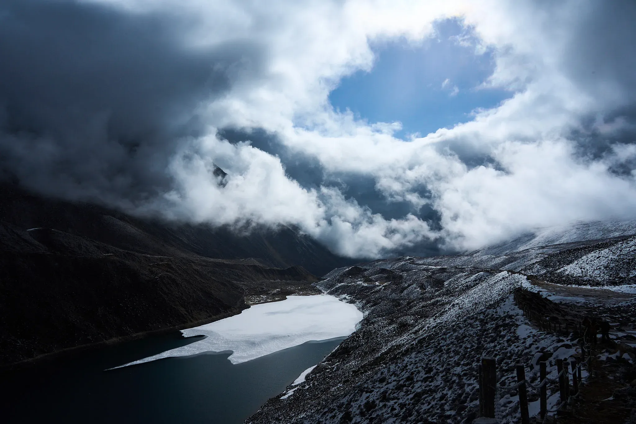 云层在雪线和冰湖上方裂开，蓝天与暗谷形成强烈的明暗入口。