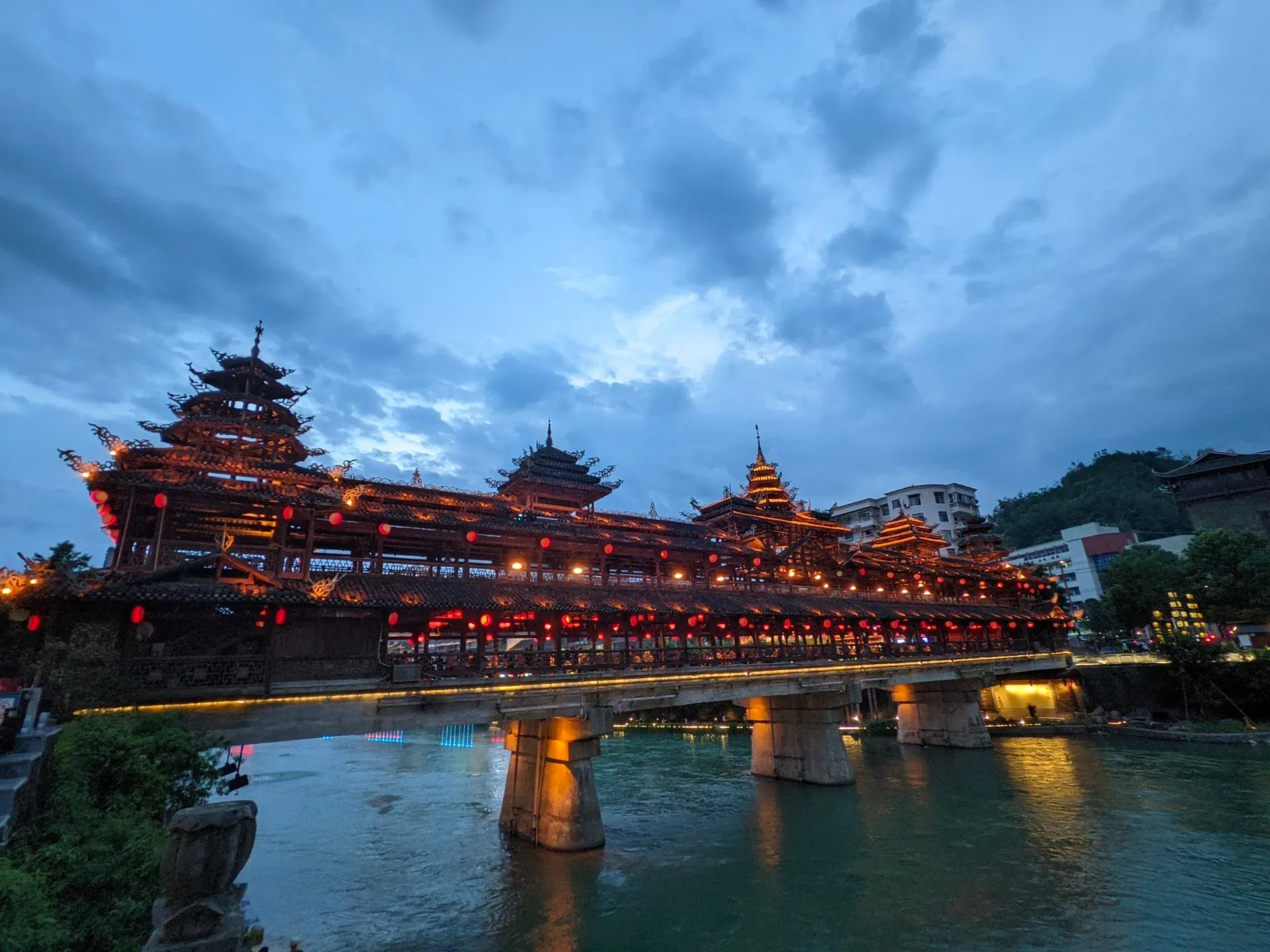 河畔楼阁在雨后亮起，灯火映入缓慢流动的水面。