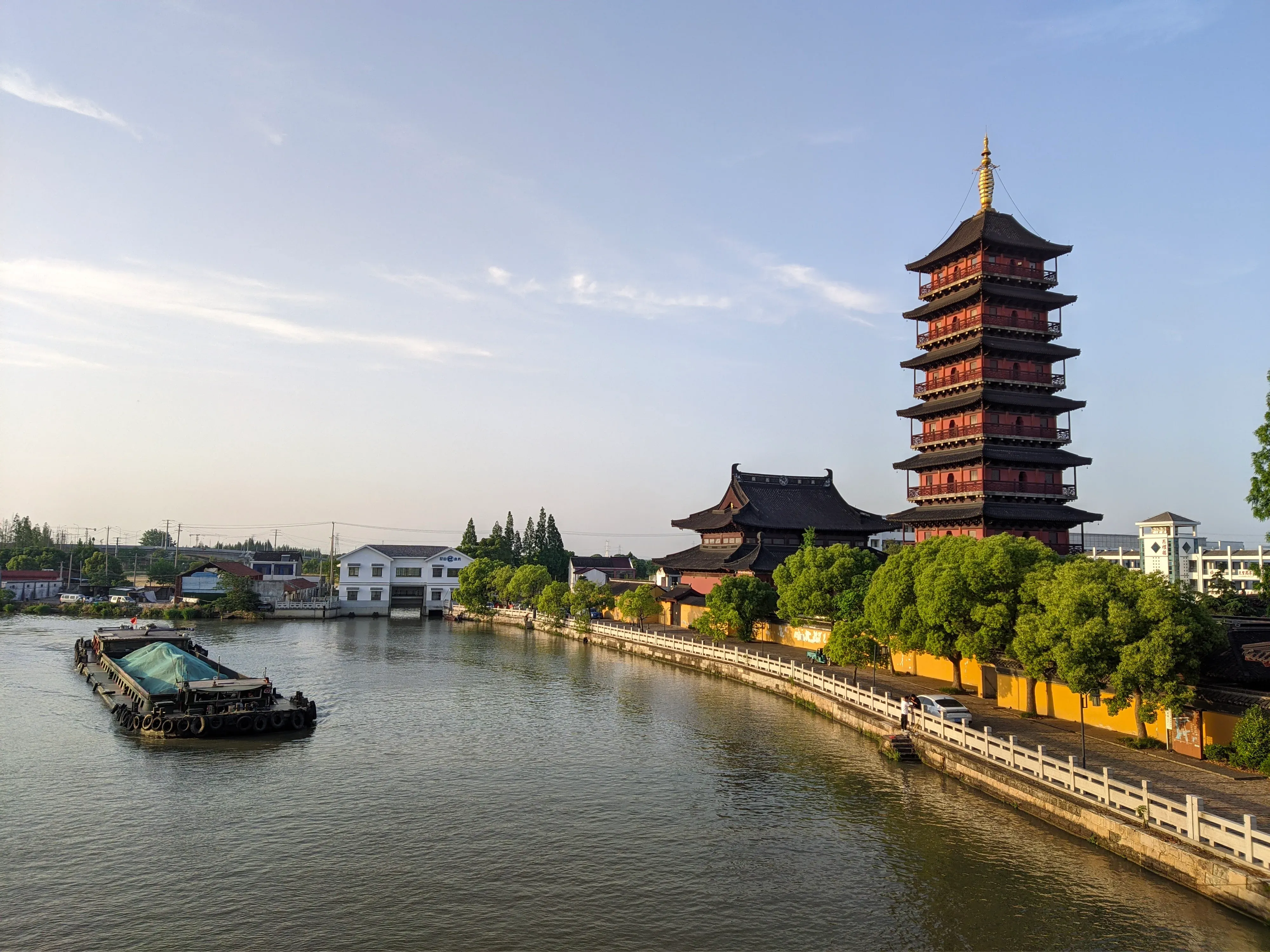 小舟经过河岸古塔，斜阳把白墙与水面染成暖色。