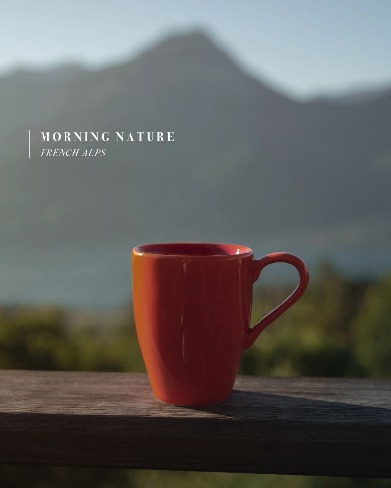 Tasse rouge sur une terrasse avec vue floue sur les montagnes des Alpes françaises au matin — photographie de voyage nature par Paul Piccolini