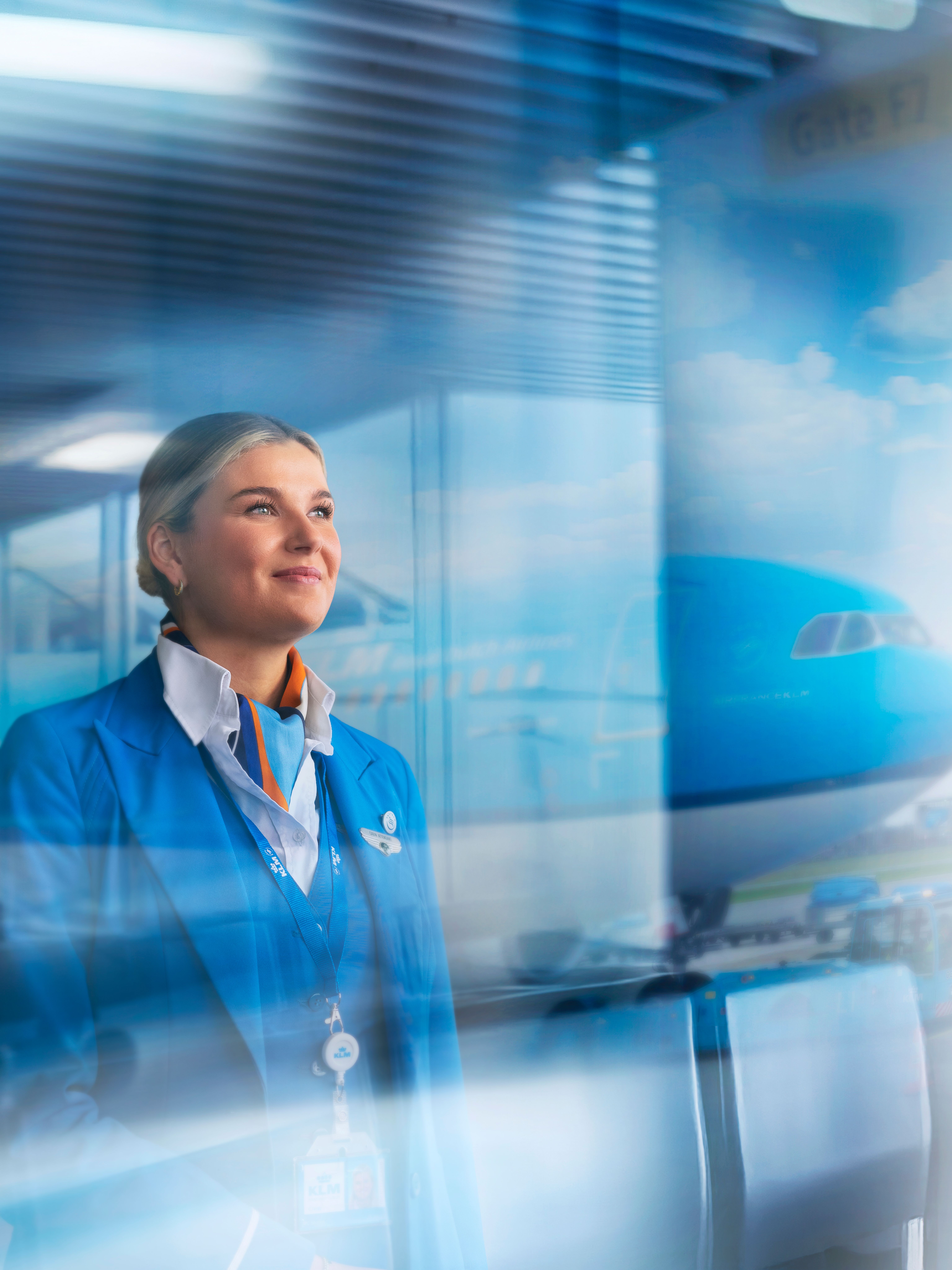 KLM cabin attendant die uit een raam kijkt met een vliegtuig op de achtergrond