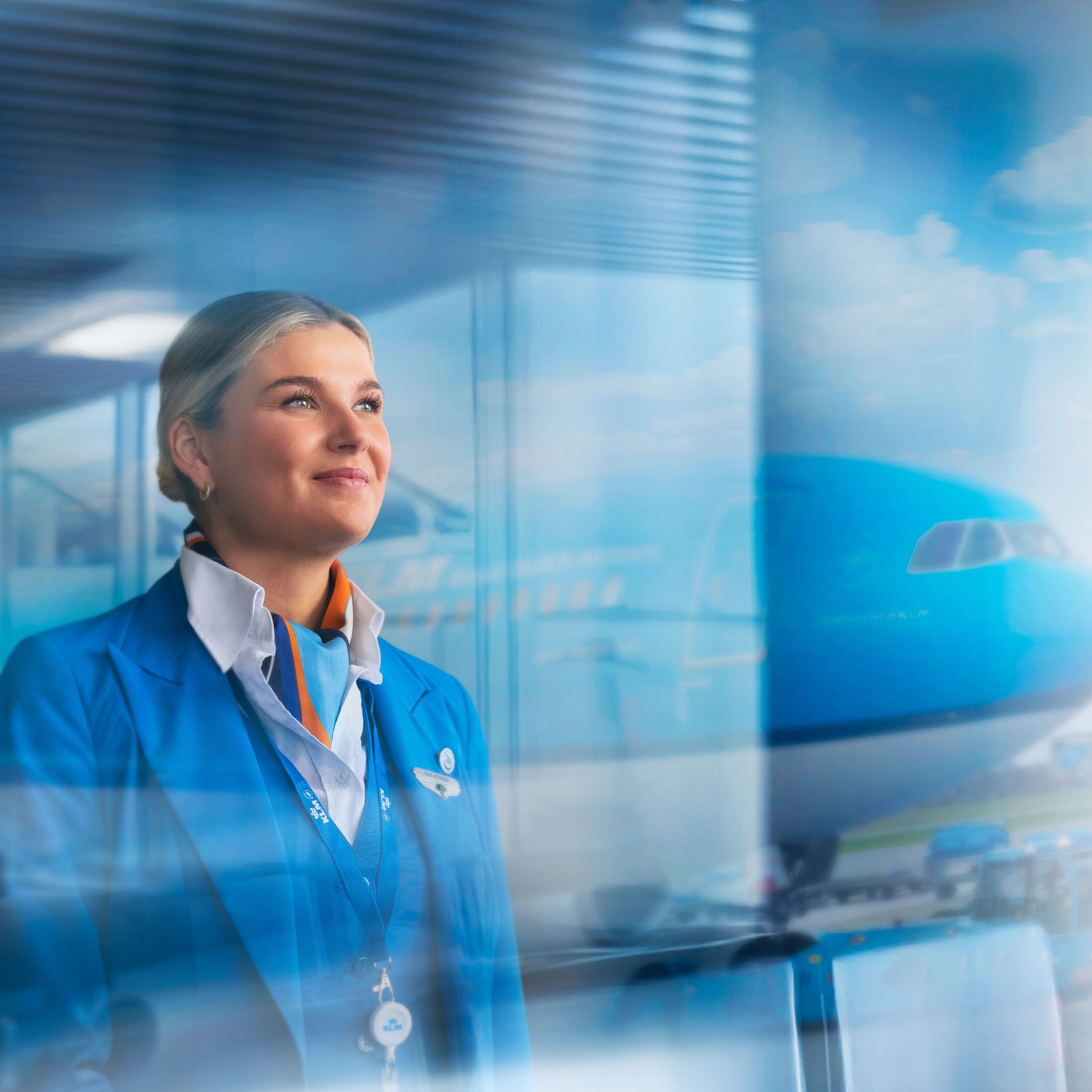 KLM cabin attendant looking out of a window with an aircraft in the background