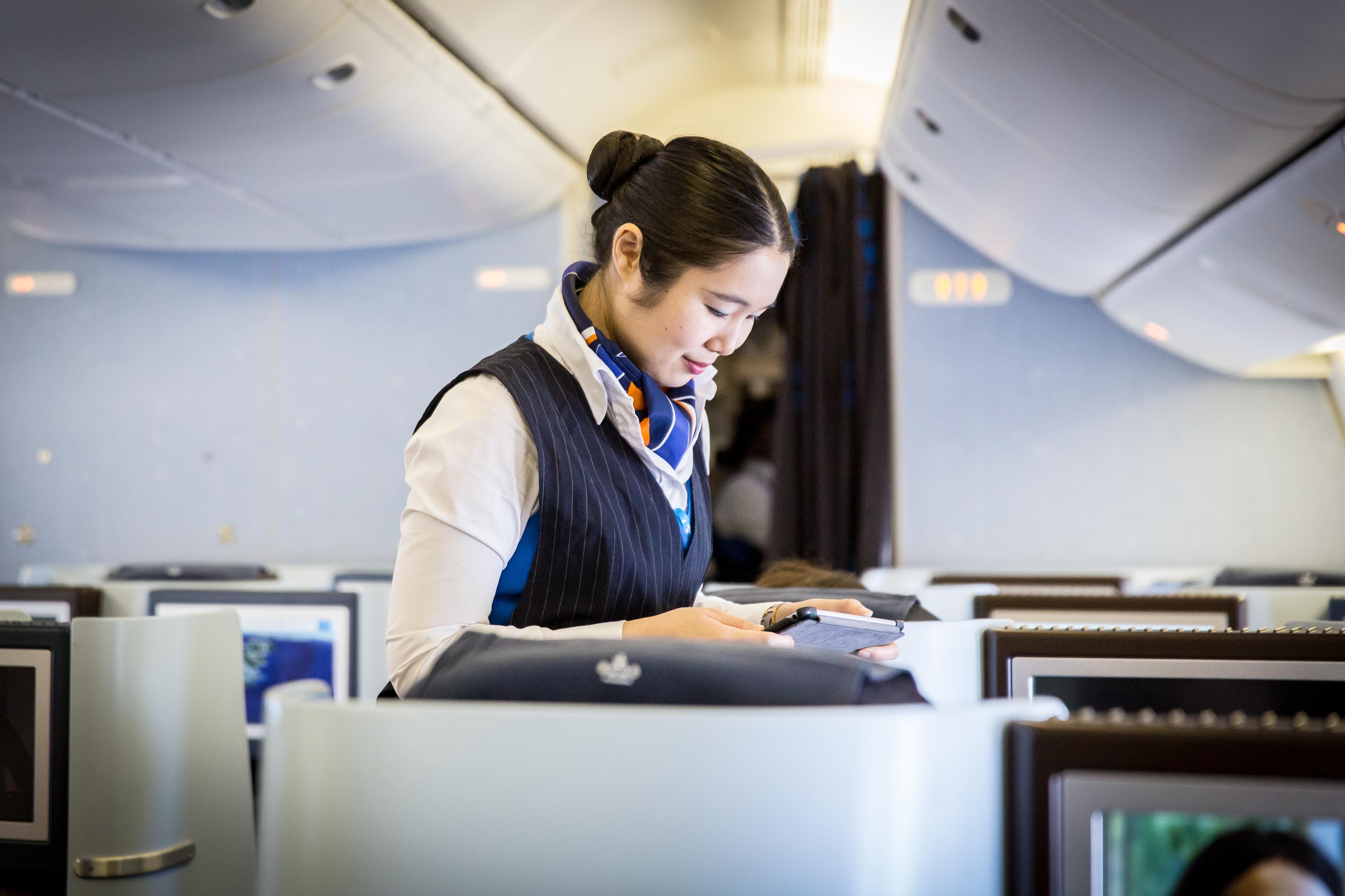 An Asian Cabin attendant taking notes on her ipad, she's working in the bussiness class