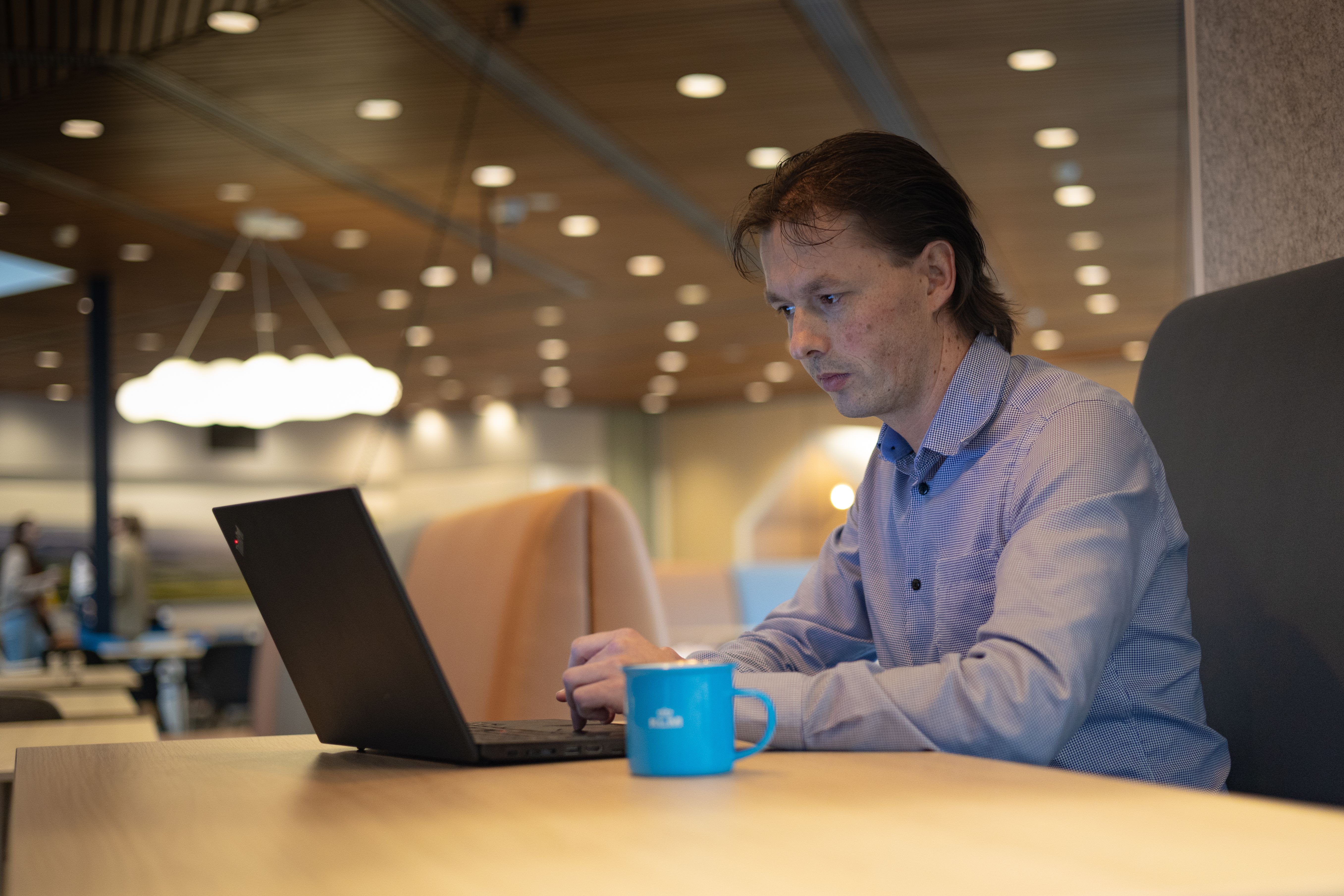 Man aan het werk op zijn laptop, met een KLM-mok naast hem