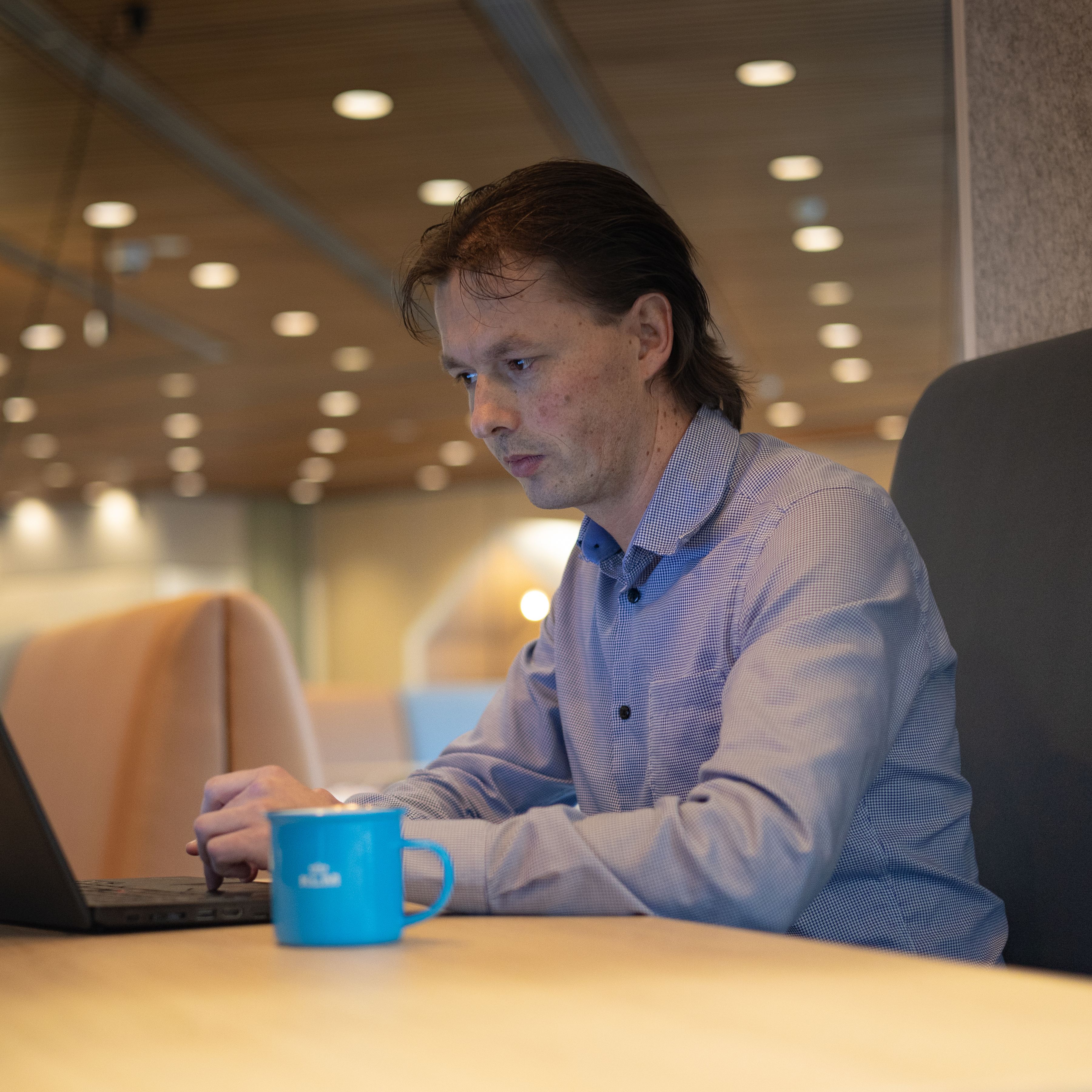 Man aan het werk op zijn laptop, met een KLM-mok naast hem