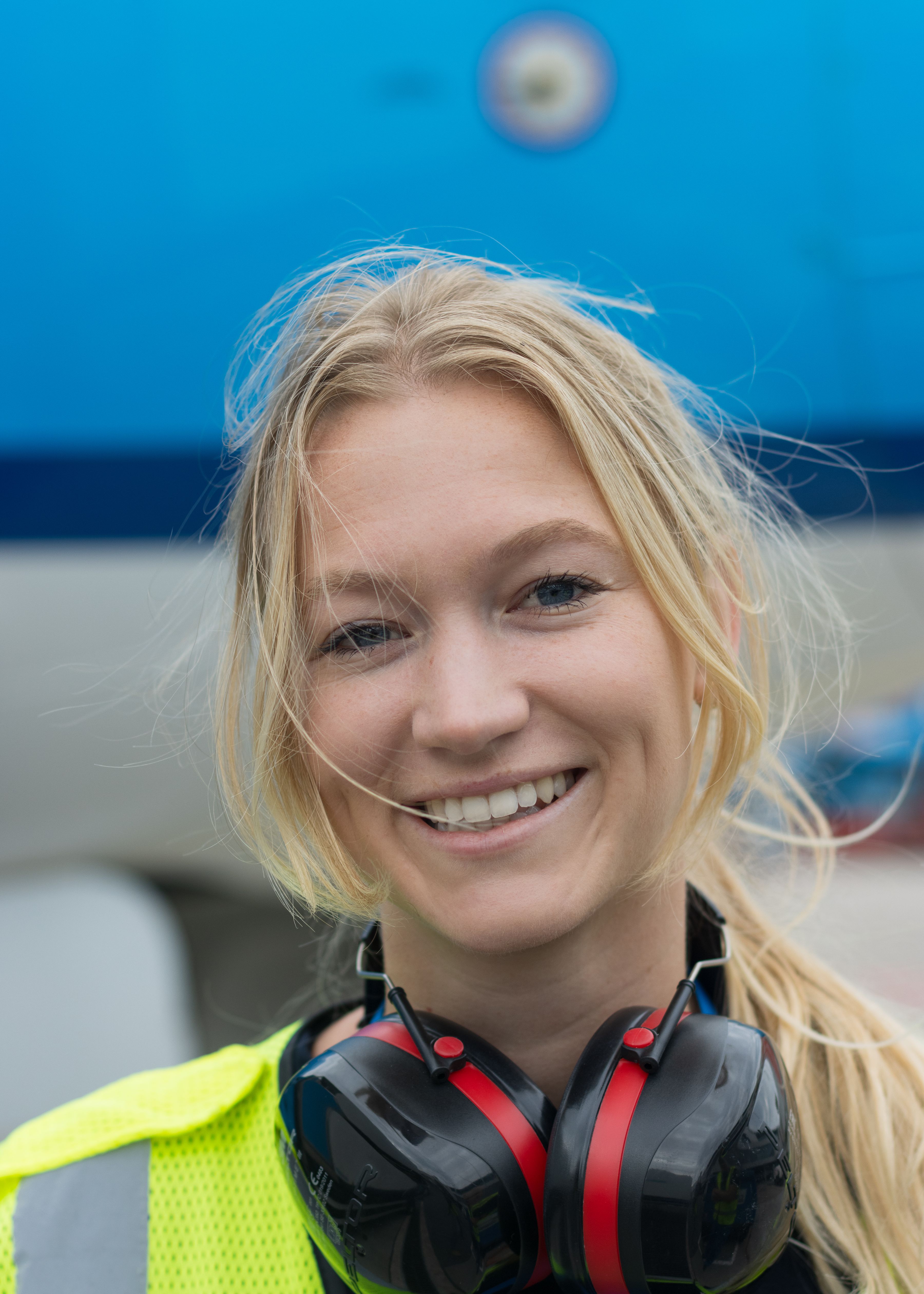 Vrouw poseert voor een vliegtuig, ze draagt beschermende werkkleding.
