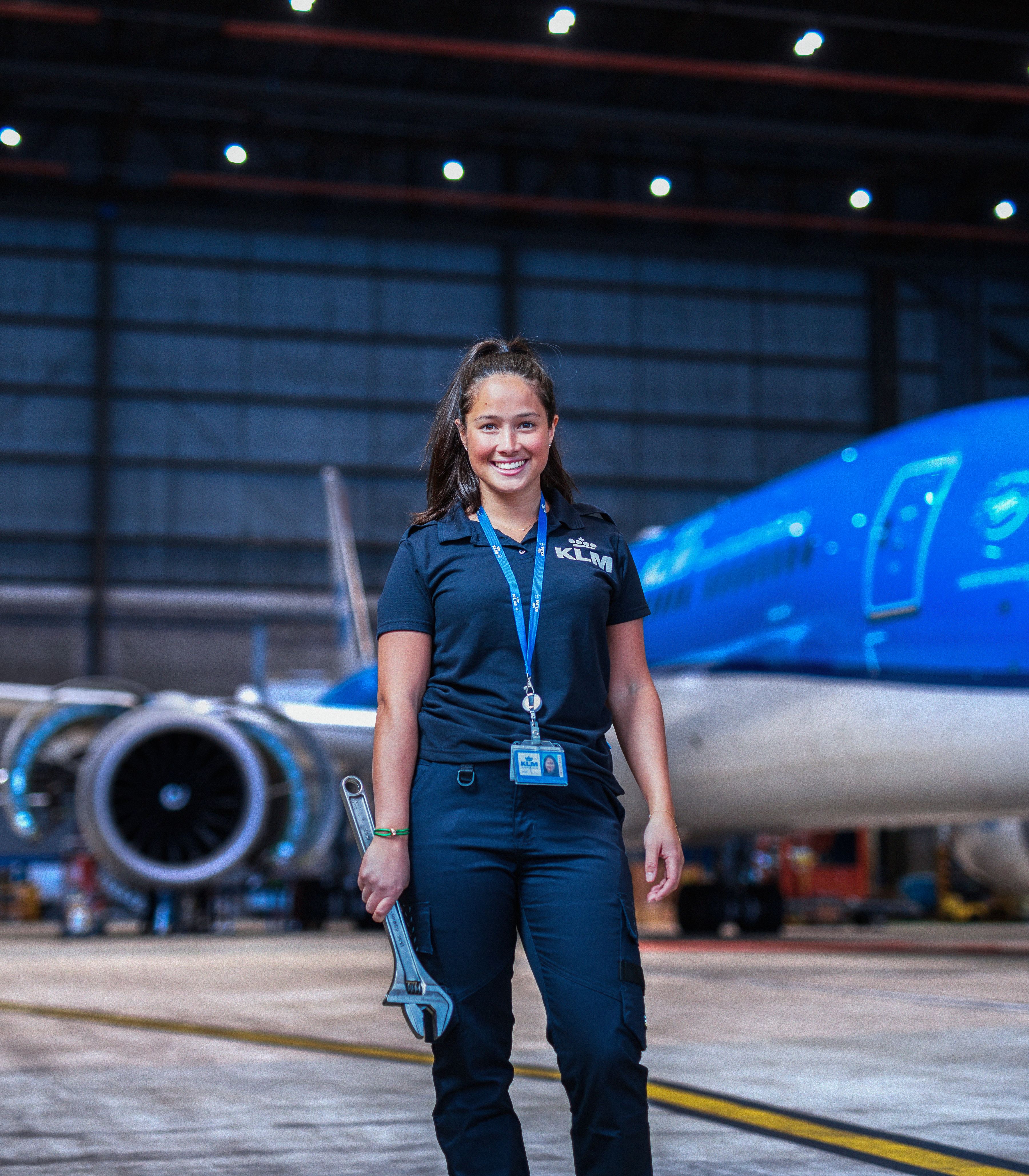 Engineering & Maintenance collega poseert voor een vliegtuig in de hangaar met een groot stuk gereedschap in haar handen.