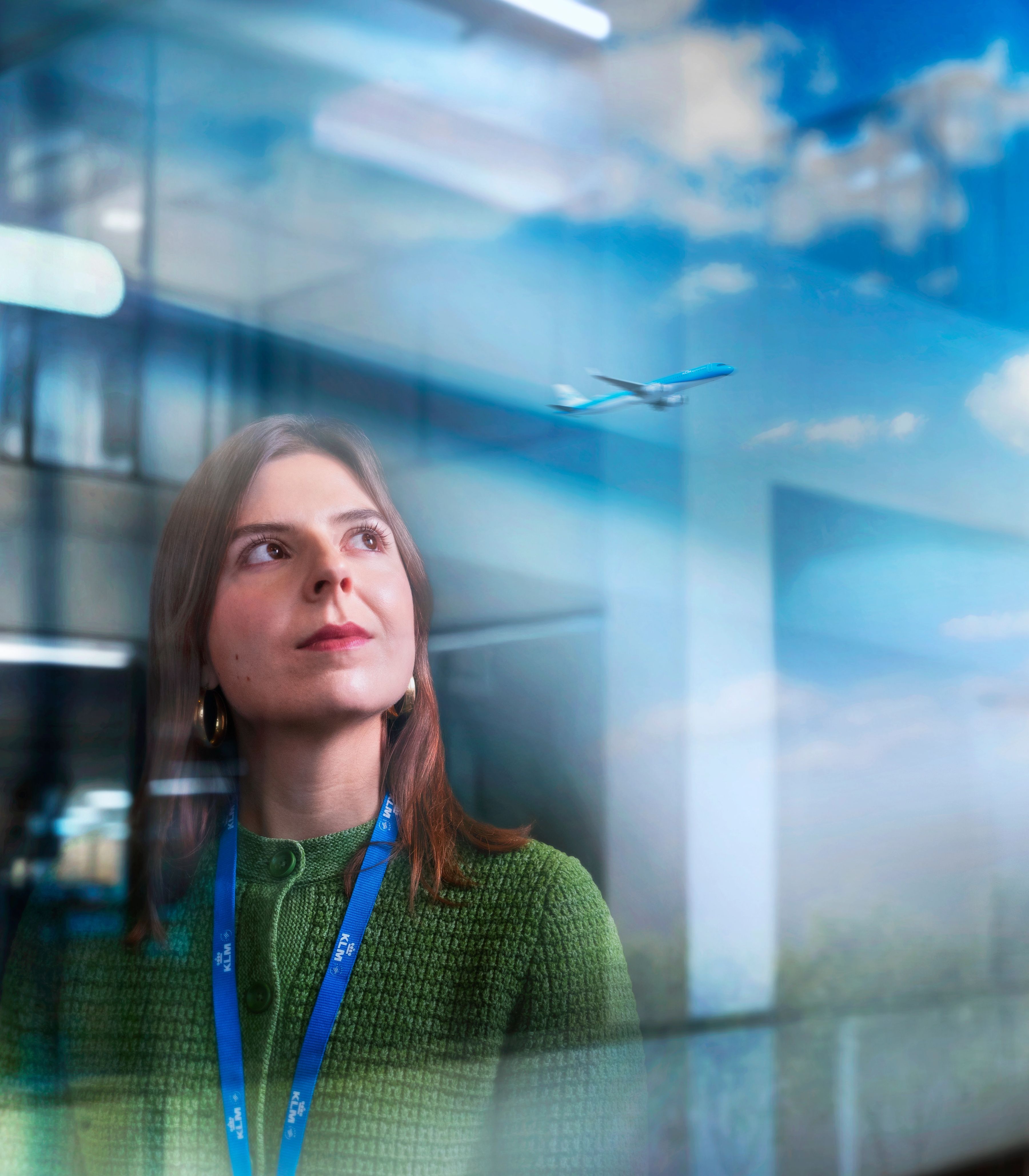 KLM-kantoor-collega staat voor een rij bomen met een blauwe lucht op de achtergrond.