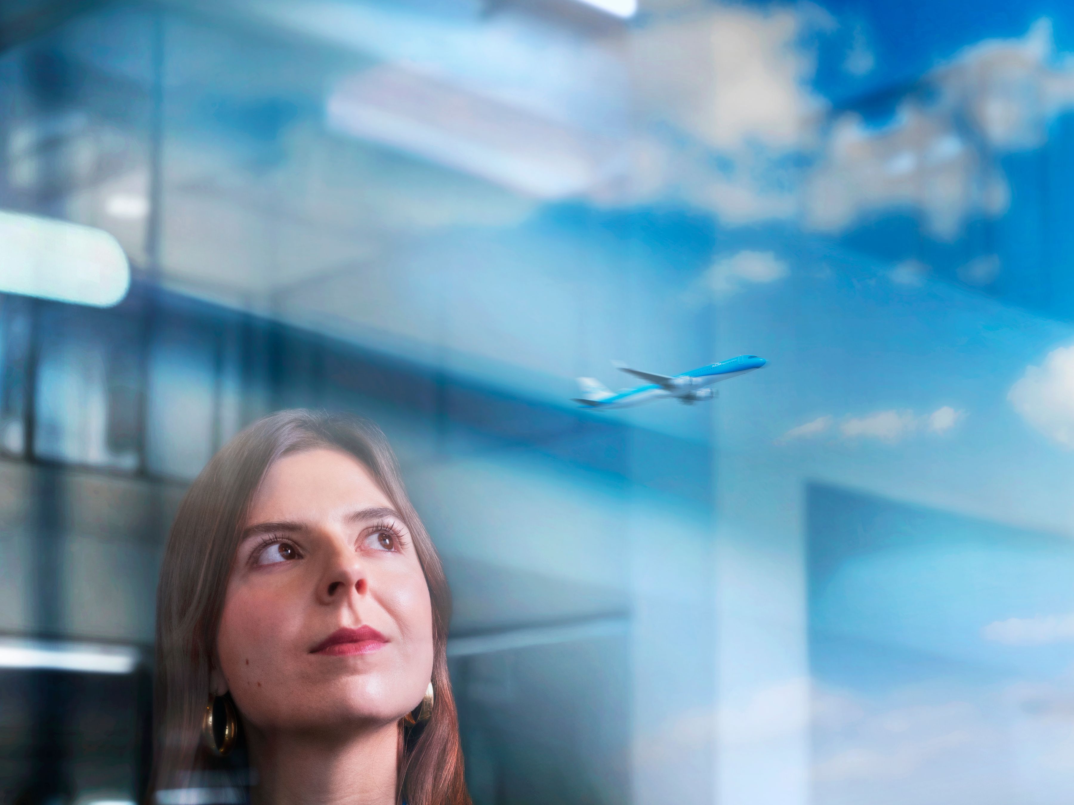 A Female KLM colleague looking out of a big window with an departing plane in the reflaction