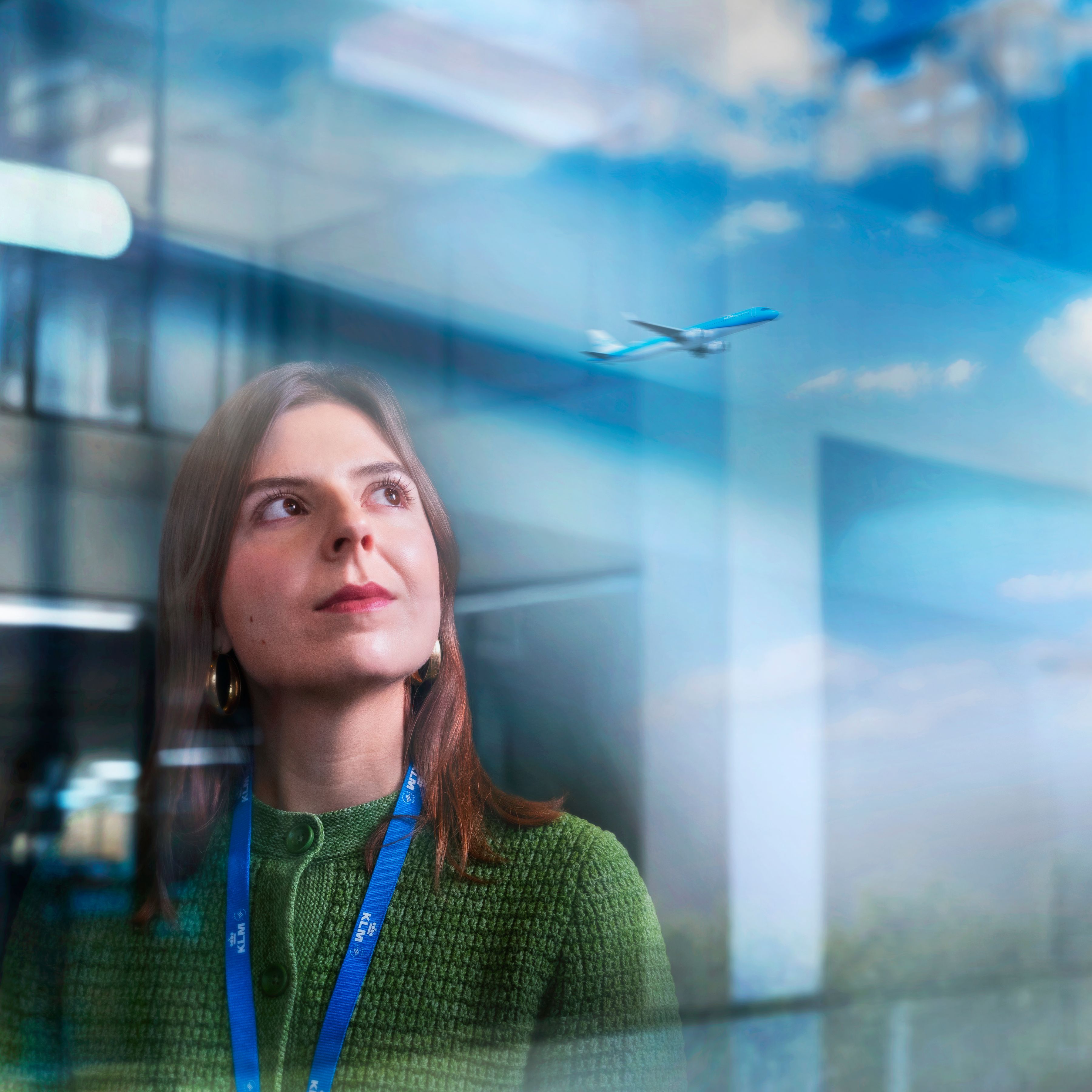 A Female KLM colleague looking out of a big window with an departing plane in the reflaction