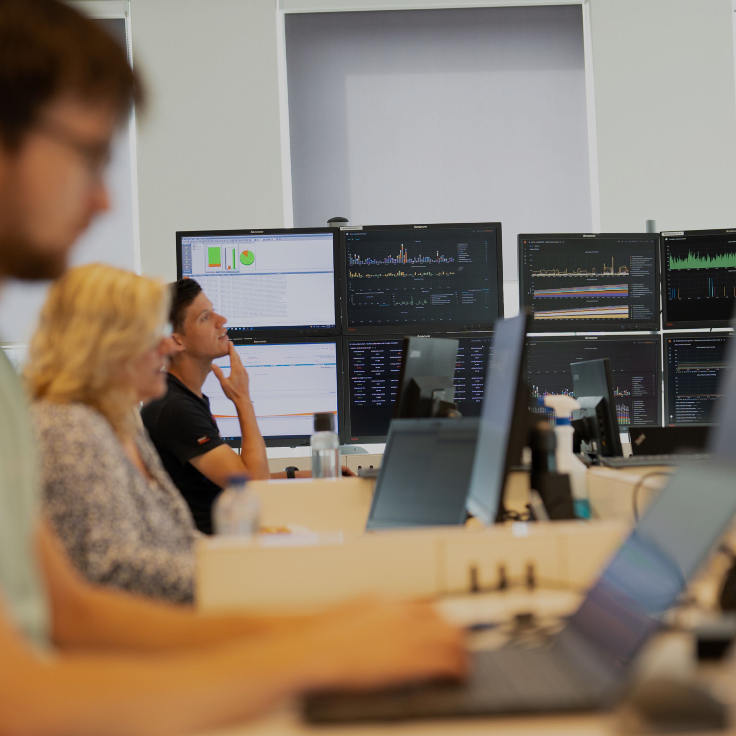 Drie KLM collega's werken achter hun laptop met meerdere schermen vol met data in de achtergrond