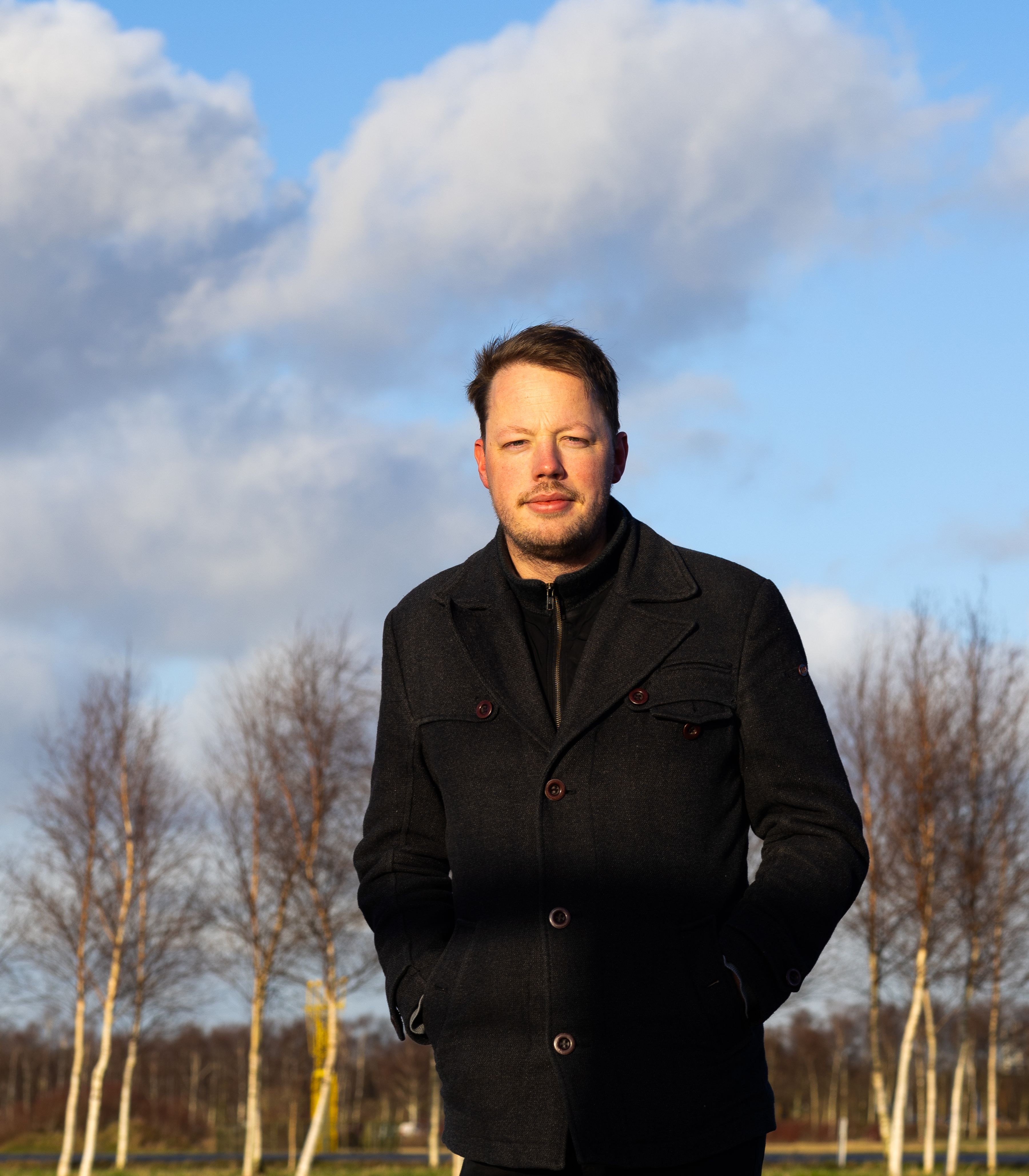 KLM office colleague standing in front of a line off trees with blue skies in the background.