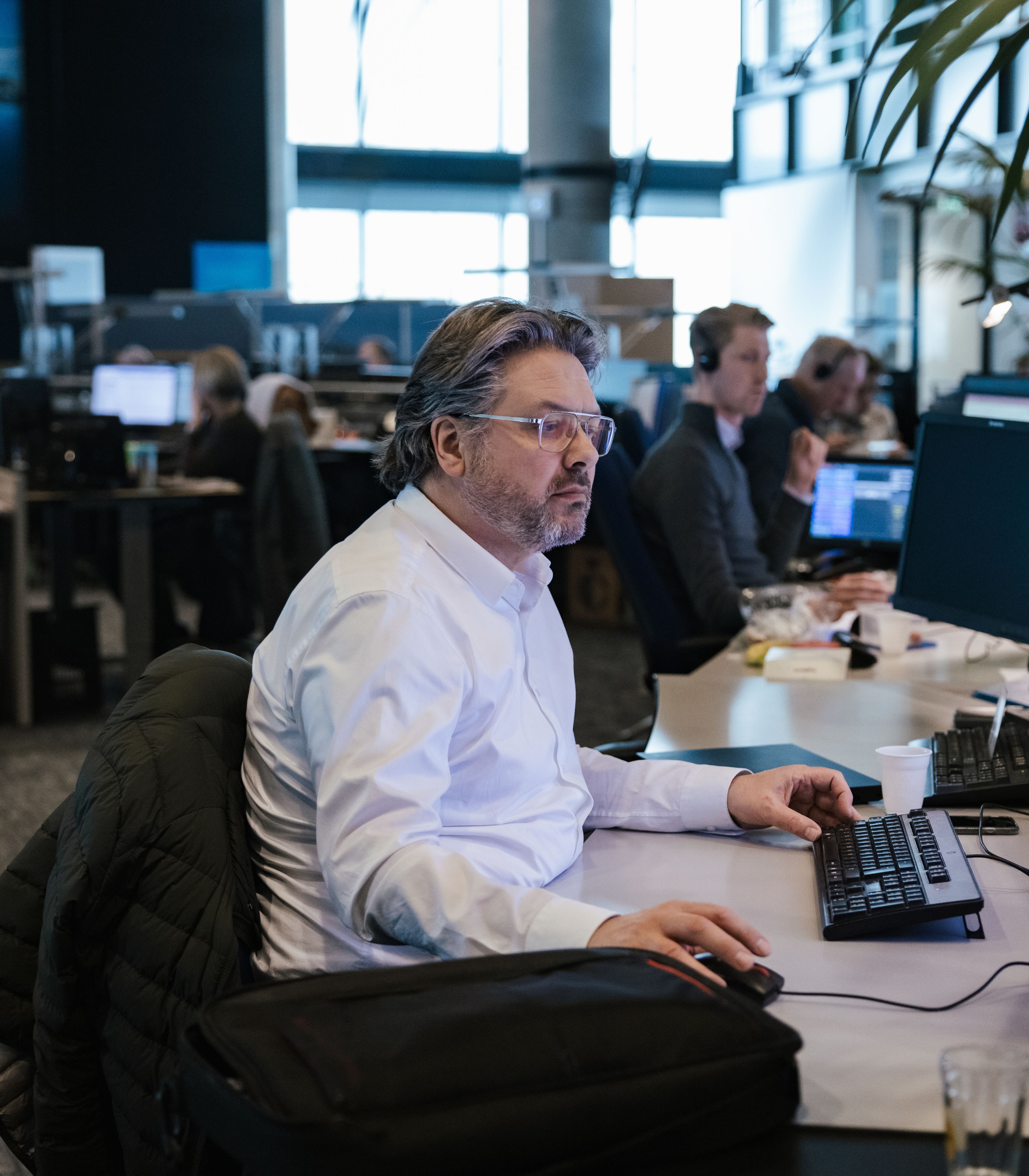 Man aan het werk achter een computer in een operations control center (OCC), met meerdere schermen en collega’s op de achtergrond