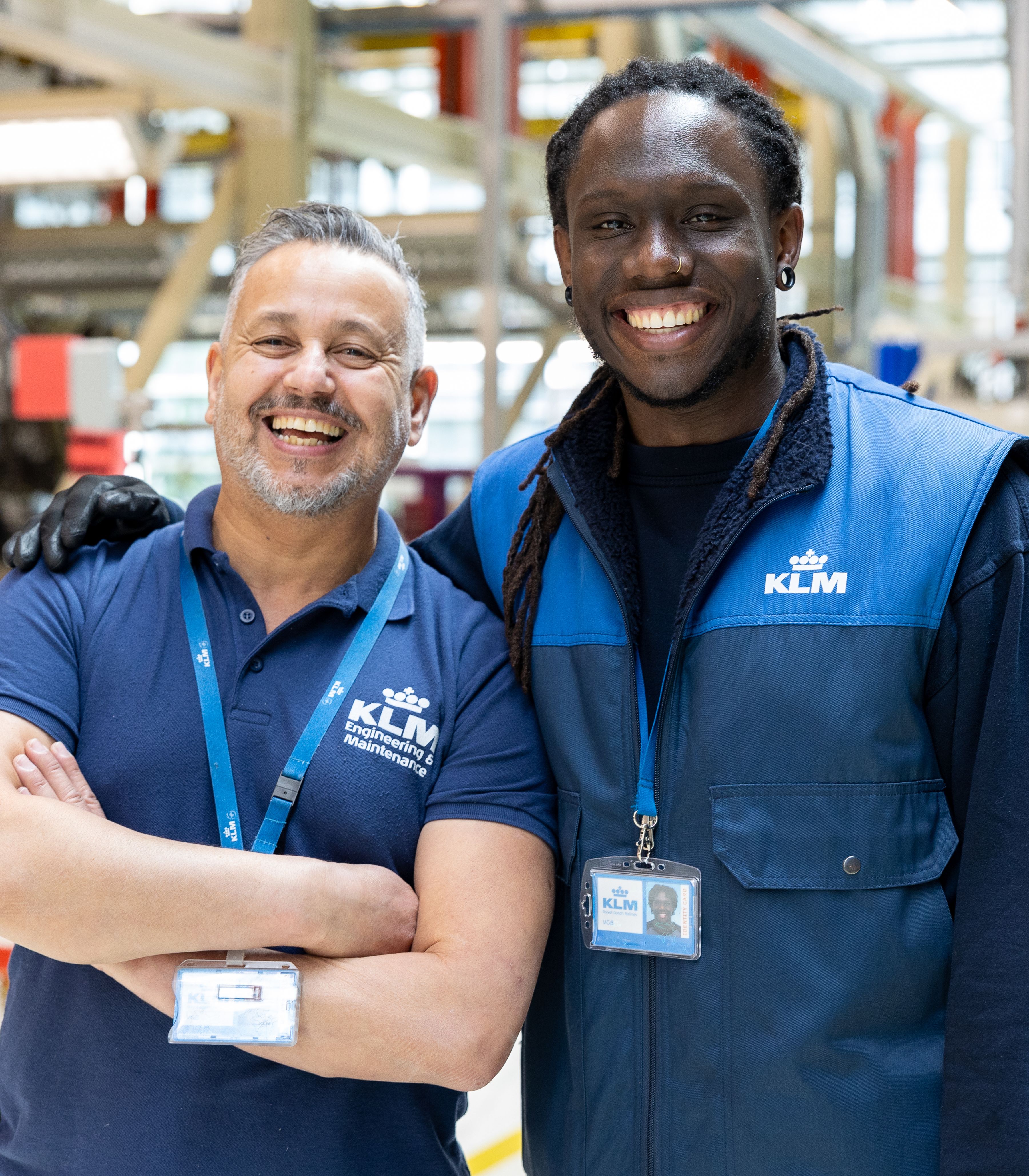 Twee lachende KLM-technici die samen in een onderhoudshangar staan.