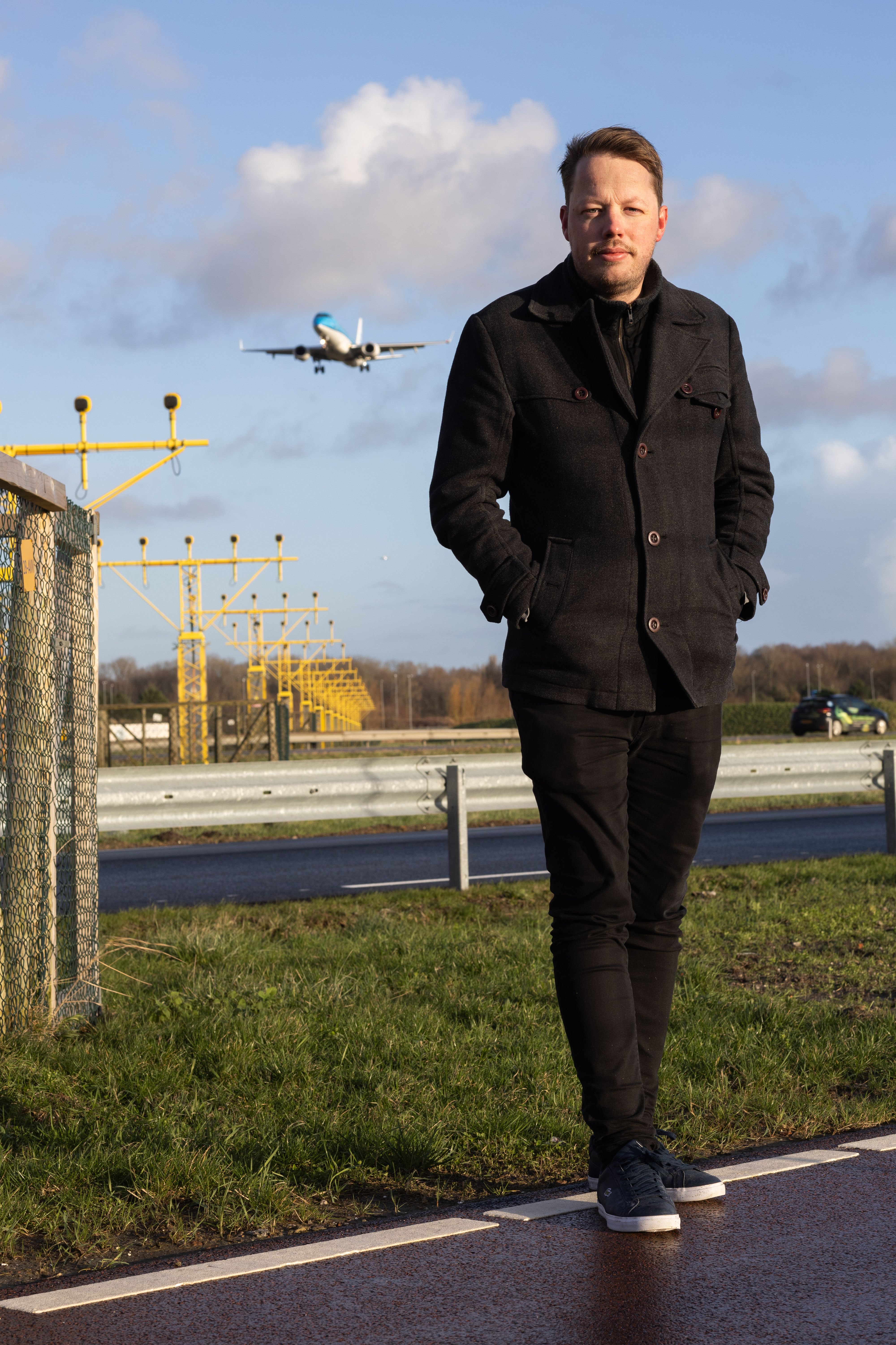 Man buiten met een landend vliegtuig op de achtergrond