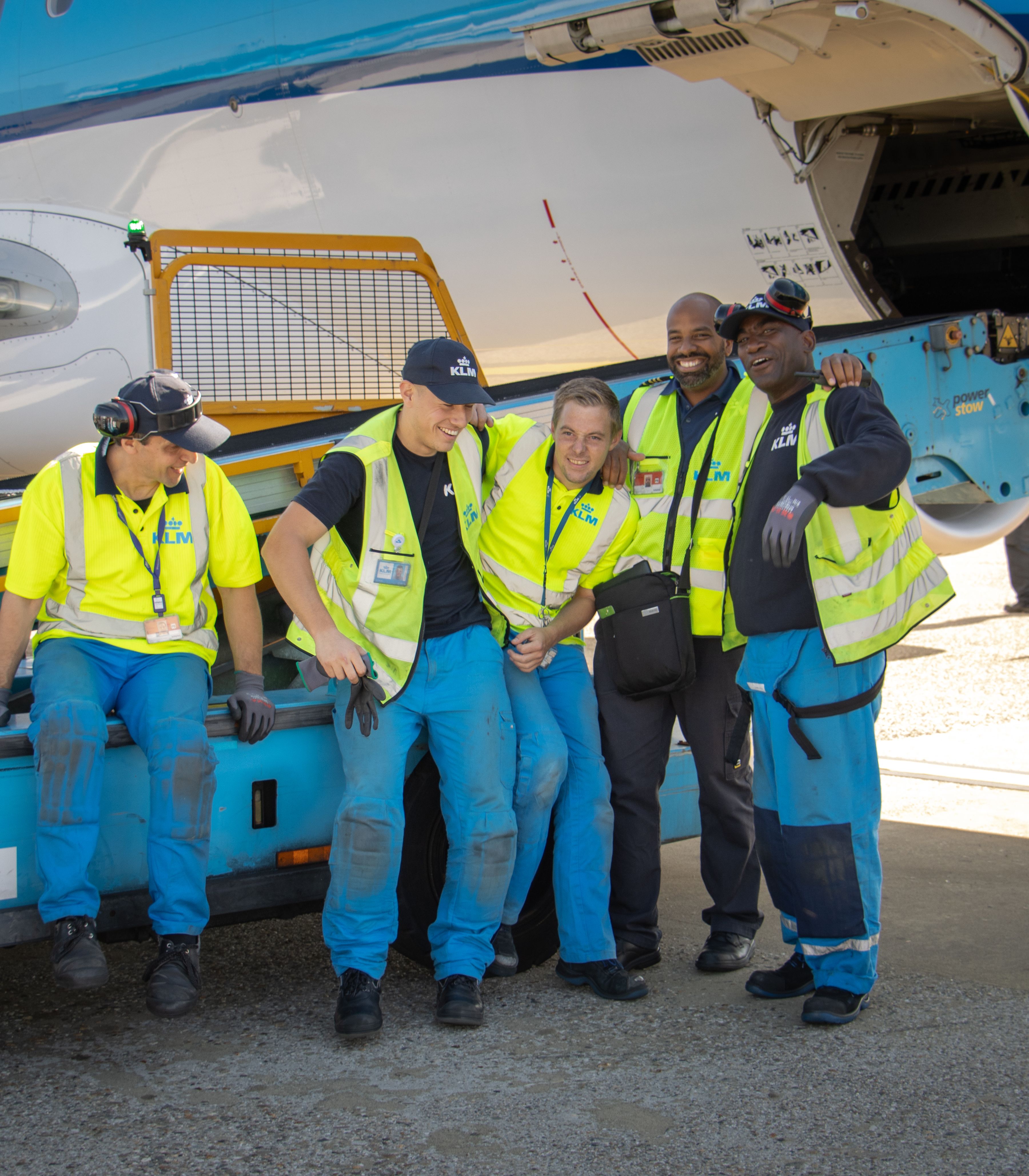 Grondoperatieteam dat samen staat in opvallende veiligheidskleding naast een KLM-vliegtuig op het platform