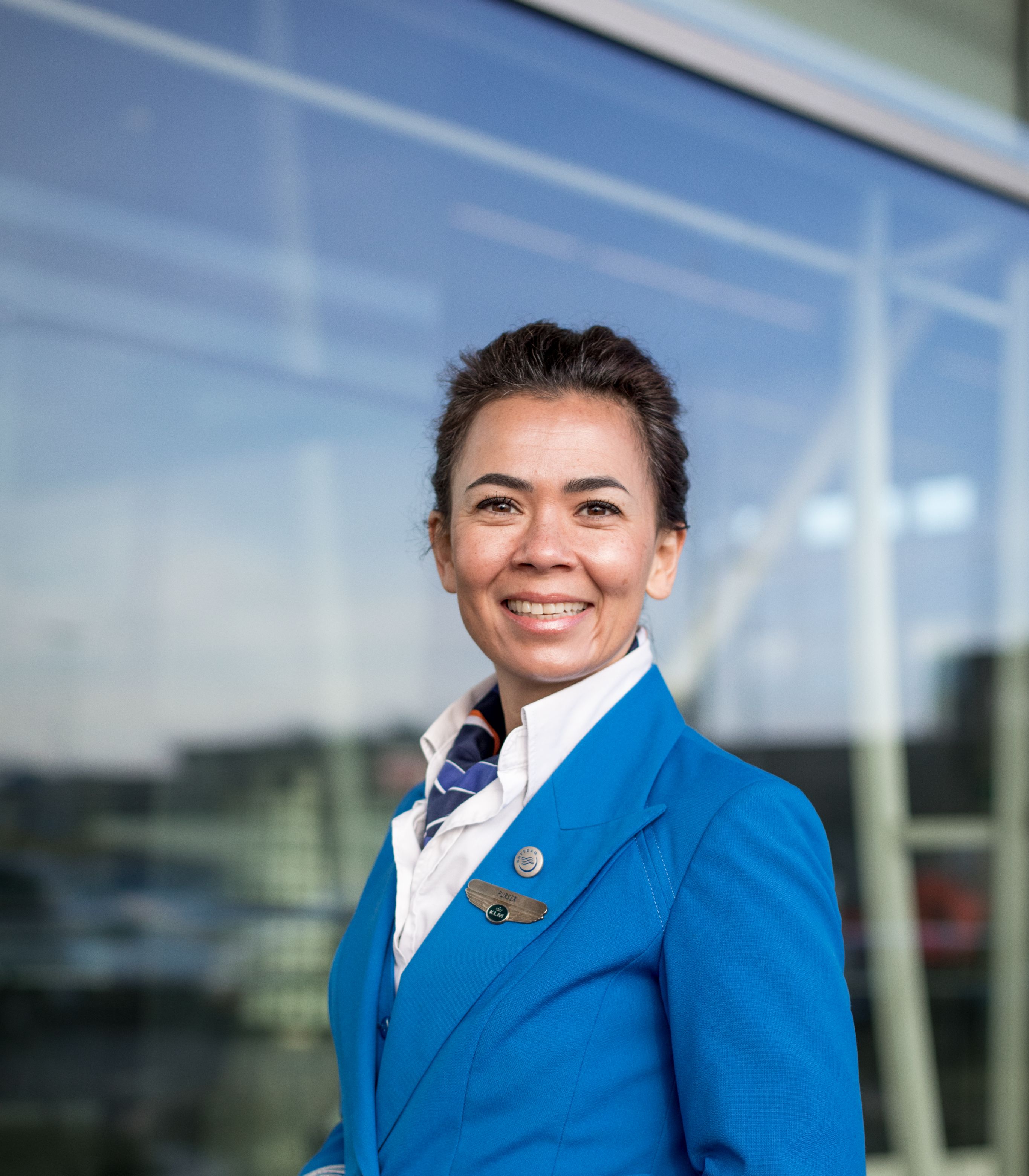 KLM-cabinepersoneelslid glimlacht en kijkt recht in de camera.
