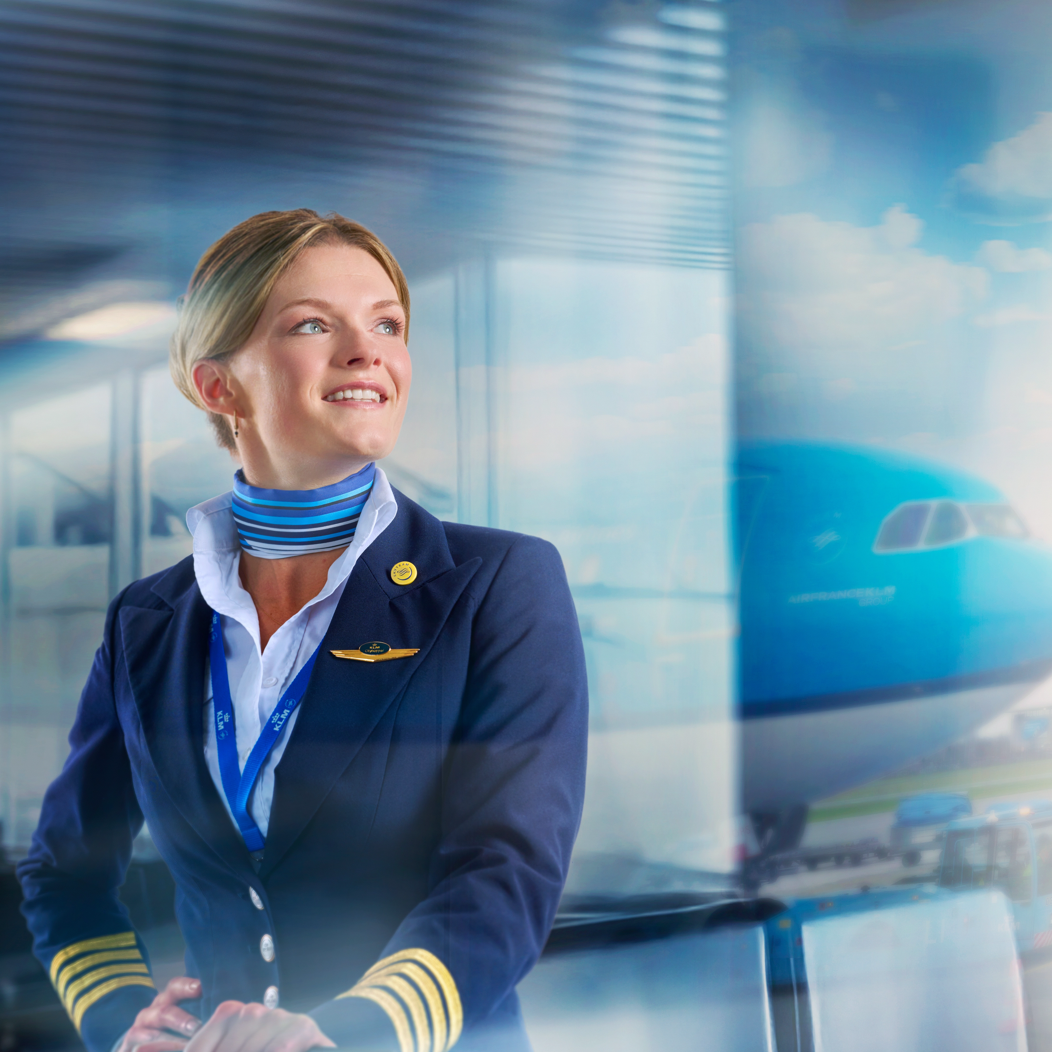 A blond woman in a pilot uniform looking out of the window on the departing plane