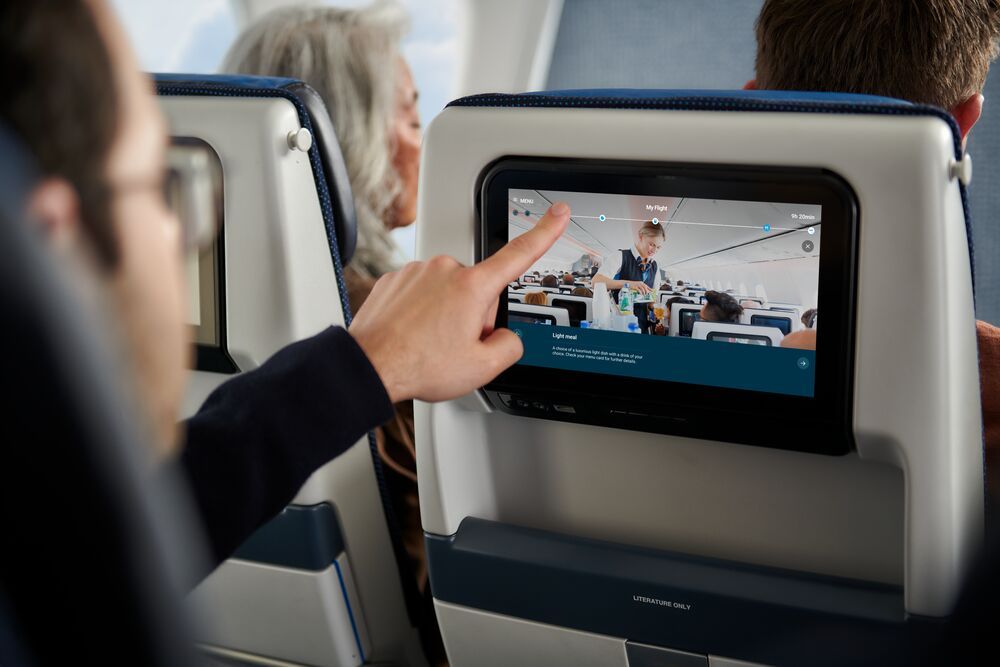 Man wijst naar scherm in stoel voor hem, aan boord van een vliegtuig