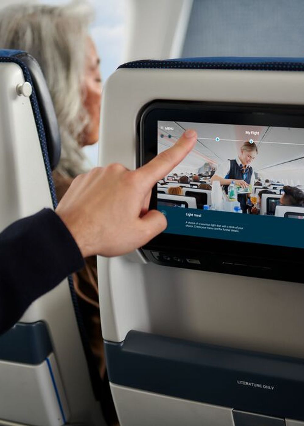 Man wijst naar scherm in stoel voor hem, aan boord van een vliegtuig