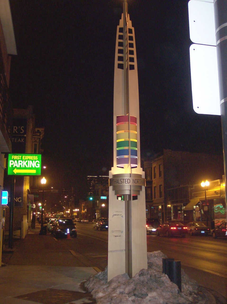 A Northalsted rainbow pylon on North Halsted at night, with rainbow rings and a snow bank at the base