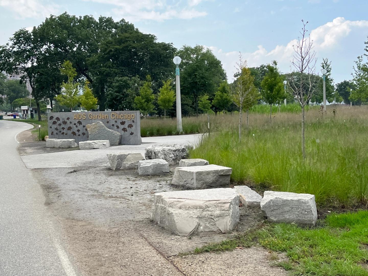 The AIDS Garden Chicago stone sign beside a lakefront path, limestone seating blocks, and prairie plantings