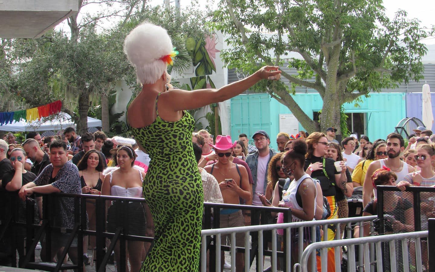 Drag performer in a green leopard dress addressing a daytime outdoor crowd at Wynwood Pride