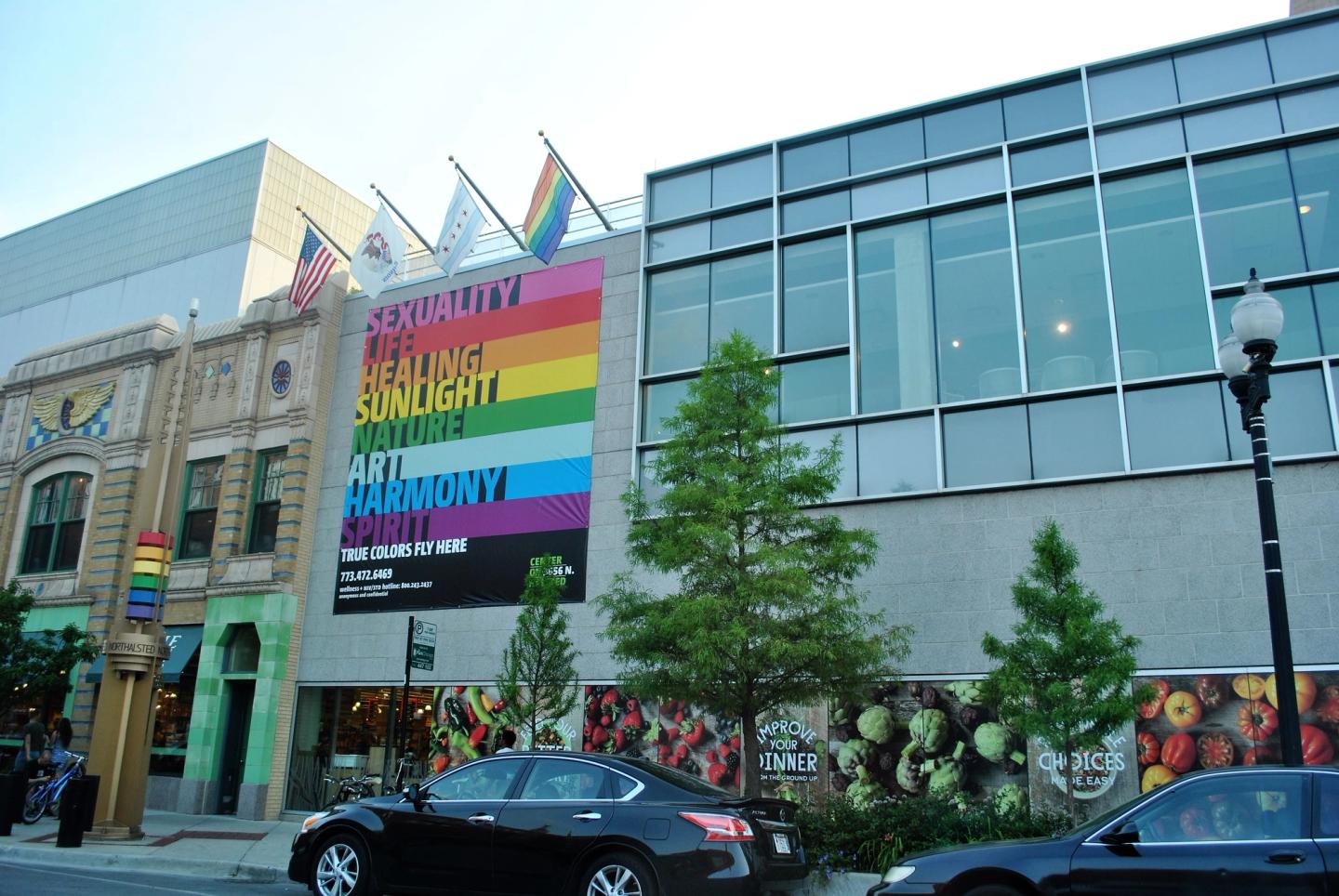 The Center on Halsted facade with a rainbow word banner, Whole Foods produce mural, and pride, city, and US flags