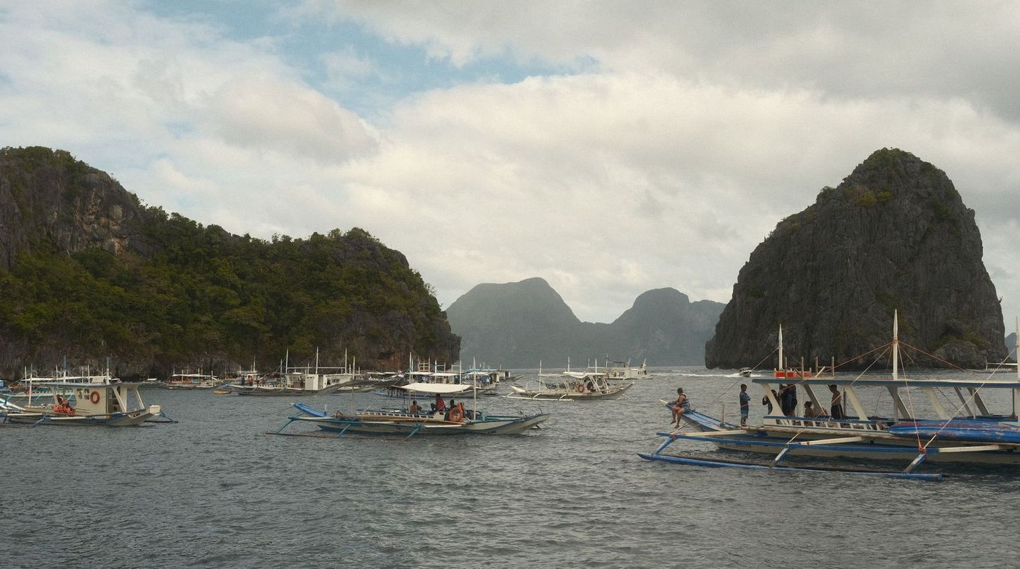 Traditional outrigger boats anchored in a Palawan bay beneath limestone cliffs
