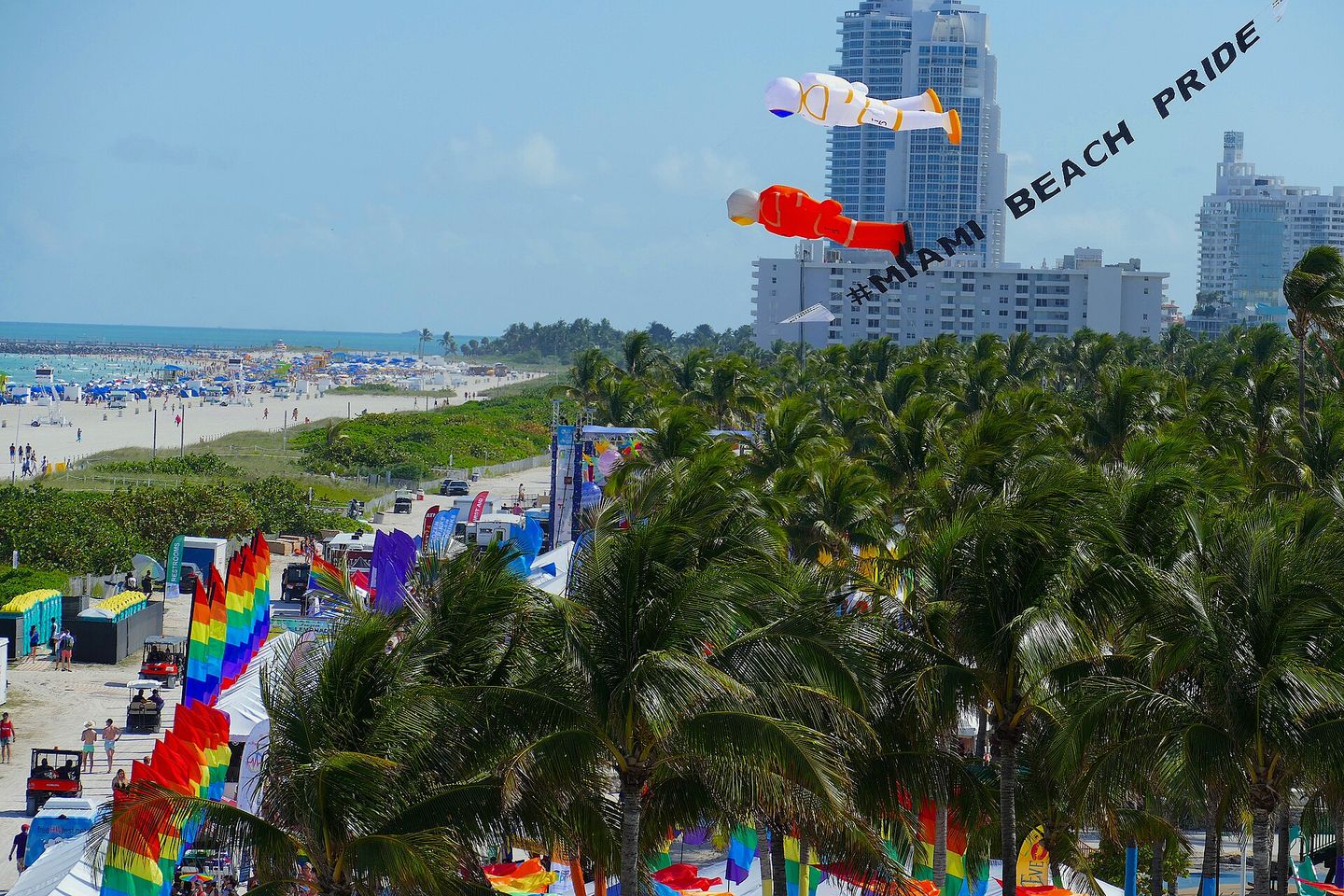 Miami Beach Pride festival at Lummus Park: rainbow flags among palms and a kite reading #MIAMI BEACH PRIDE
