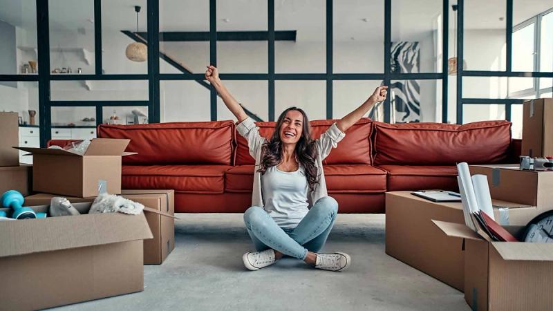 Une femme est heureuse dans son salon entourée de cartons de déménagement.