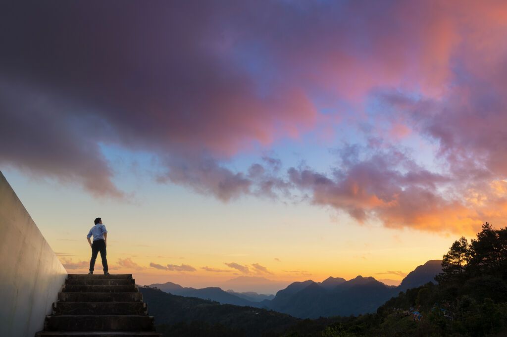 Ein Mann steht auf einer Treppe und blickt über ein Bergpanorama bei Sonnenuntergang