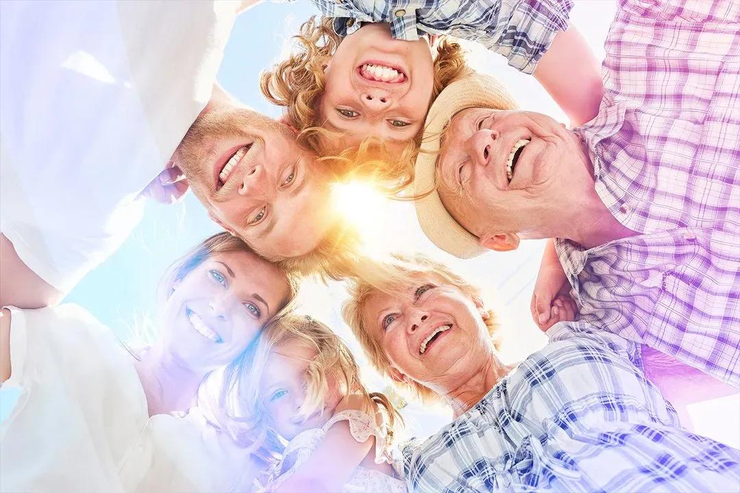 Drei Generationen einer Familie stecken lachend die Köpfe zusammen, von unten gegen die Sonne fotografiert
